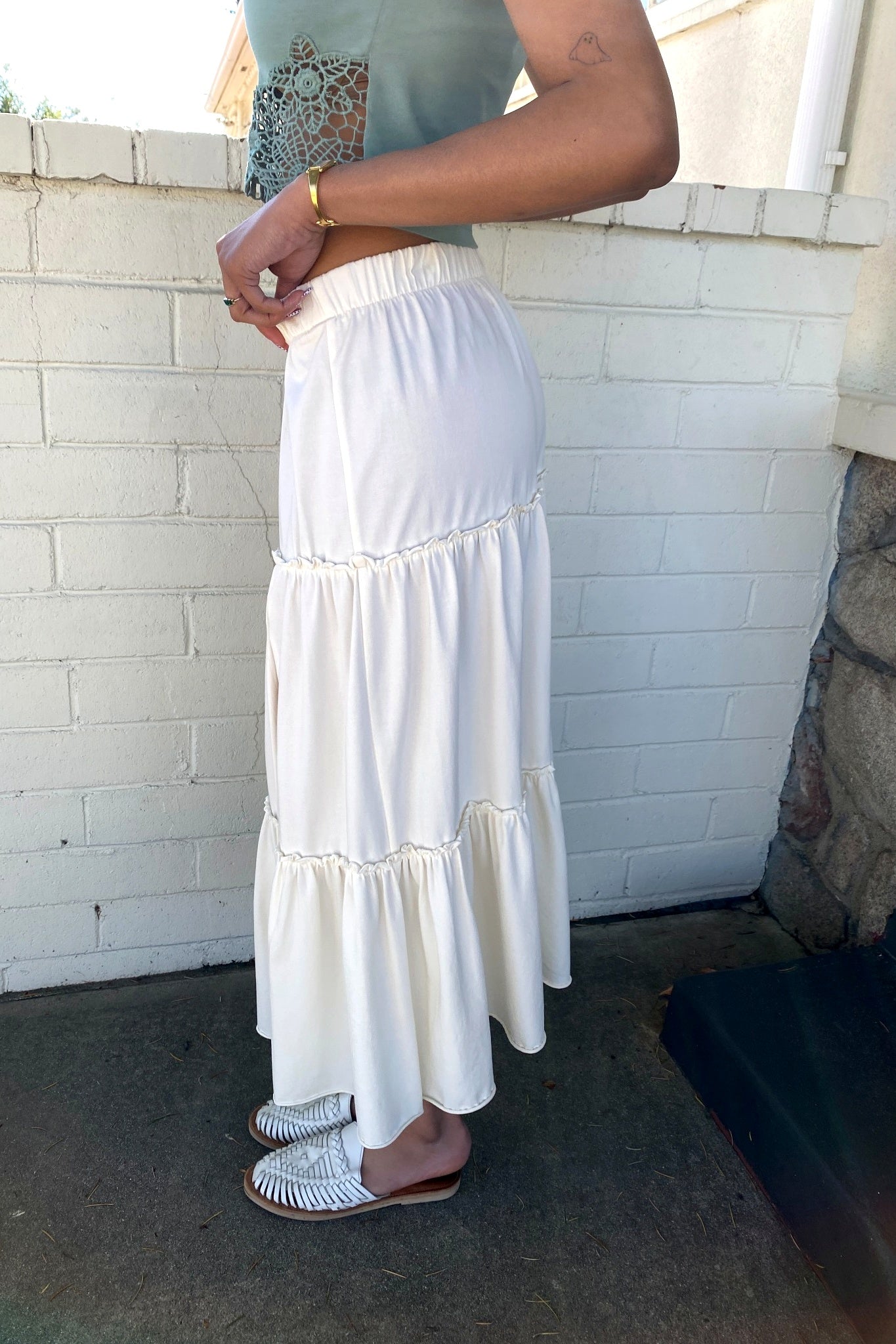 Person wearing a white tiered skirt with a light blue top against a white brick wall.