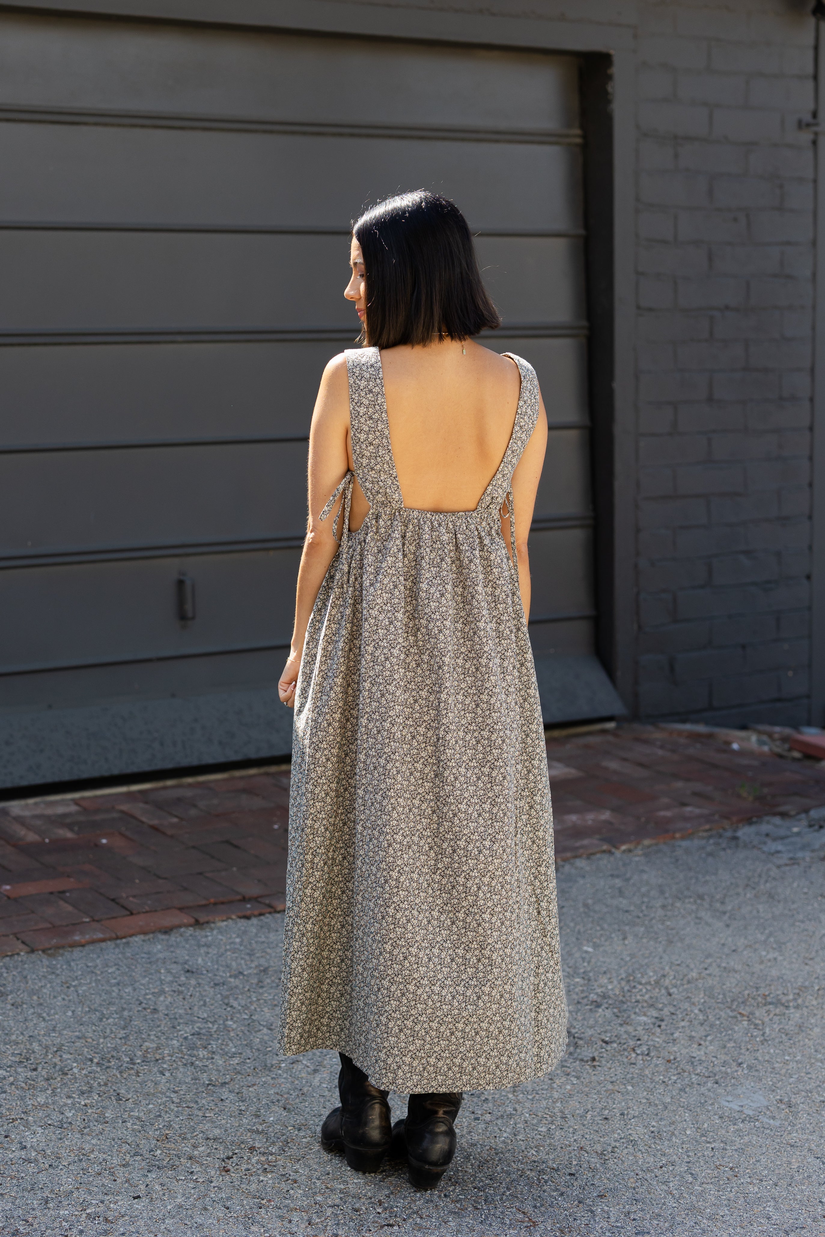 Woman wearing a long, patterned dress with an open back, standing in front of a garage.