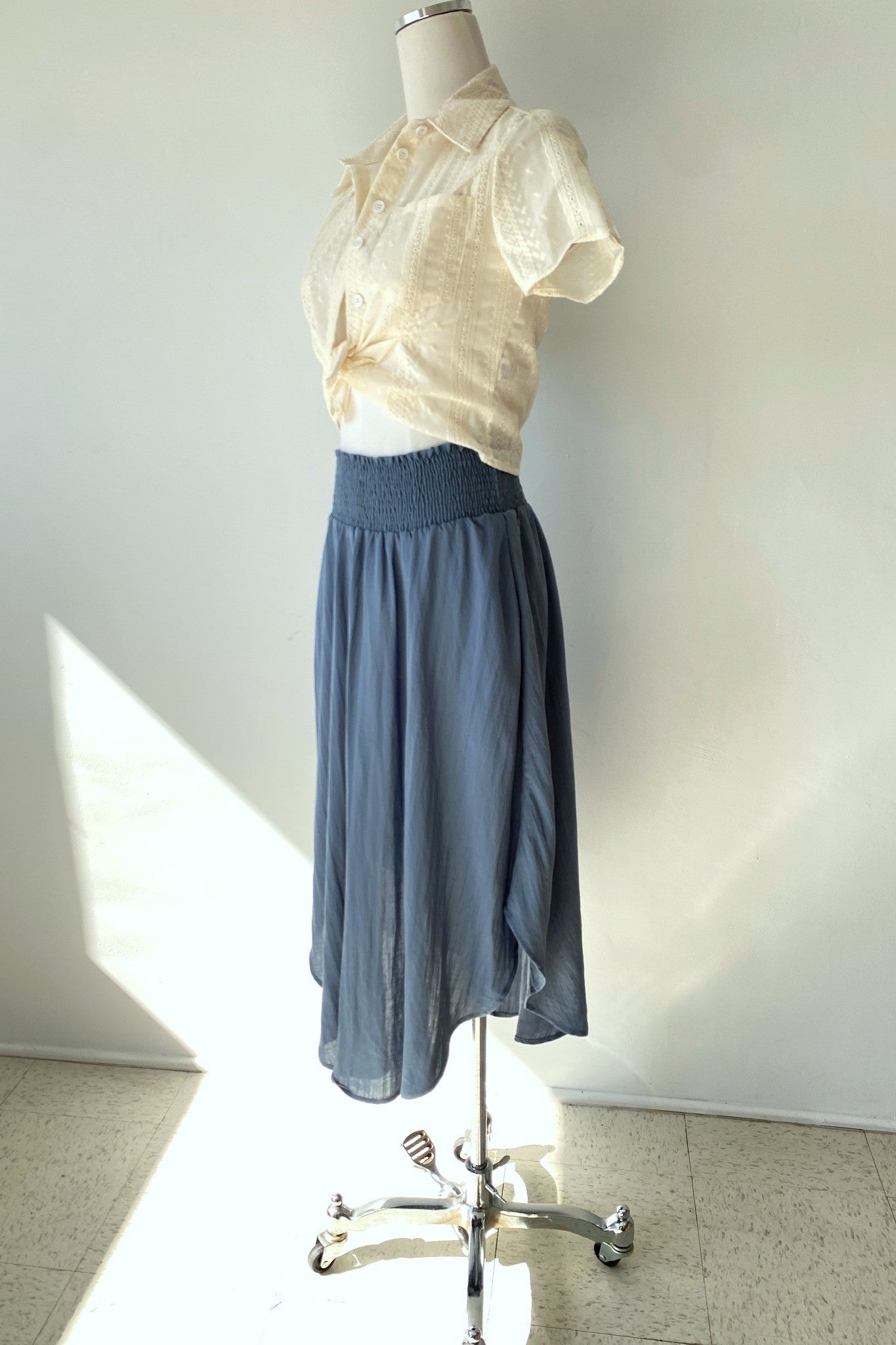 Mannequin wearing a light-colored blouse and blue skirt against a white wall.