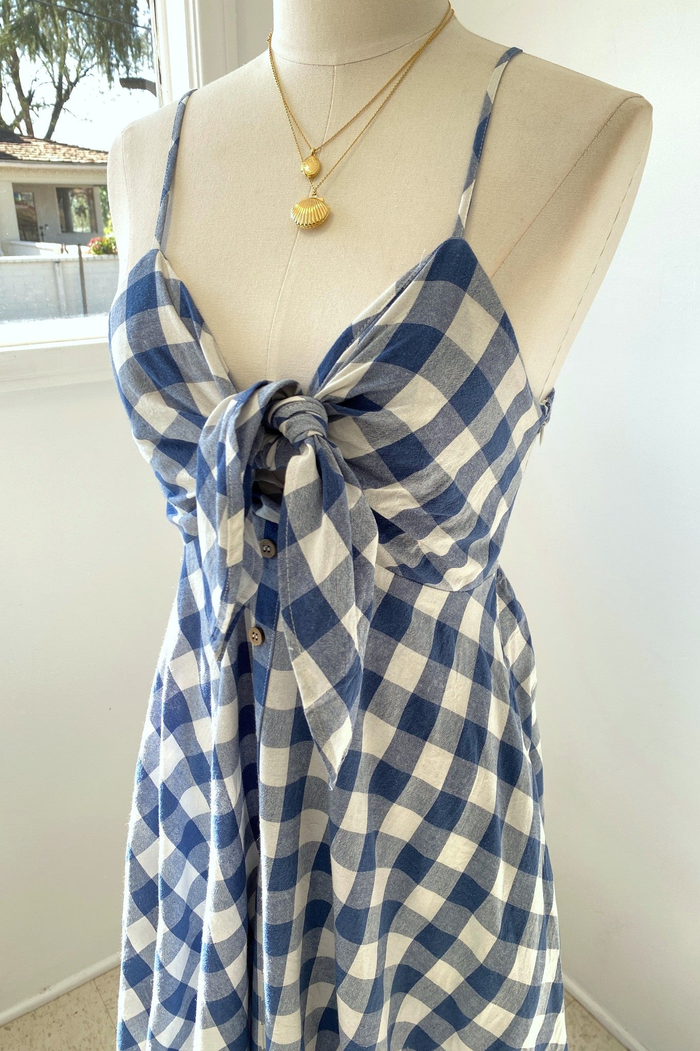 Blue and white checkered dress on a mannequin with a gold necklace.