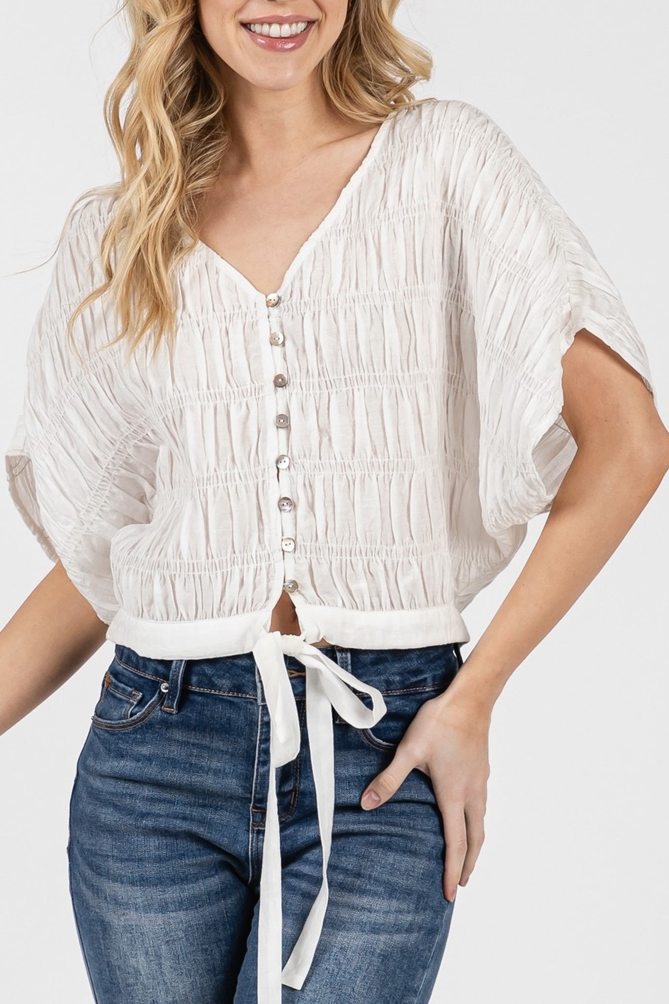 Woman wearing a white blouse with ruffled sleeves and blue jeans on a white background