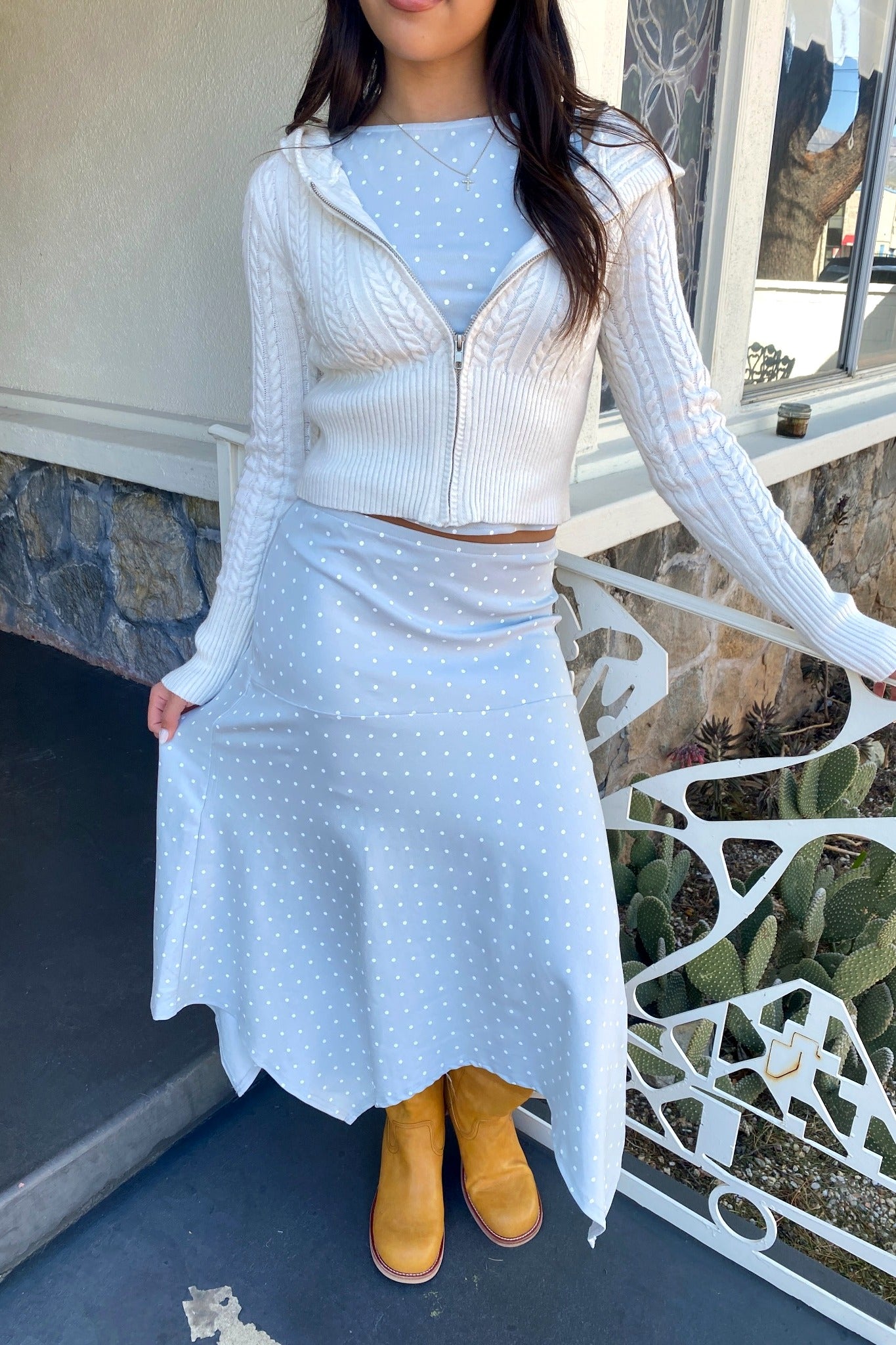Woman wearing a light blue polka dot outfit with a white cardigan on a porch.