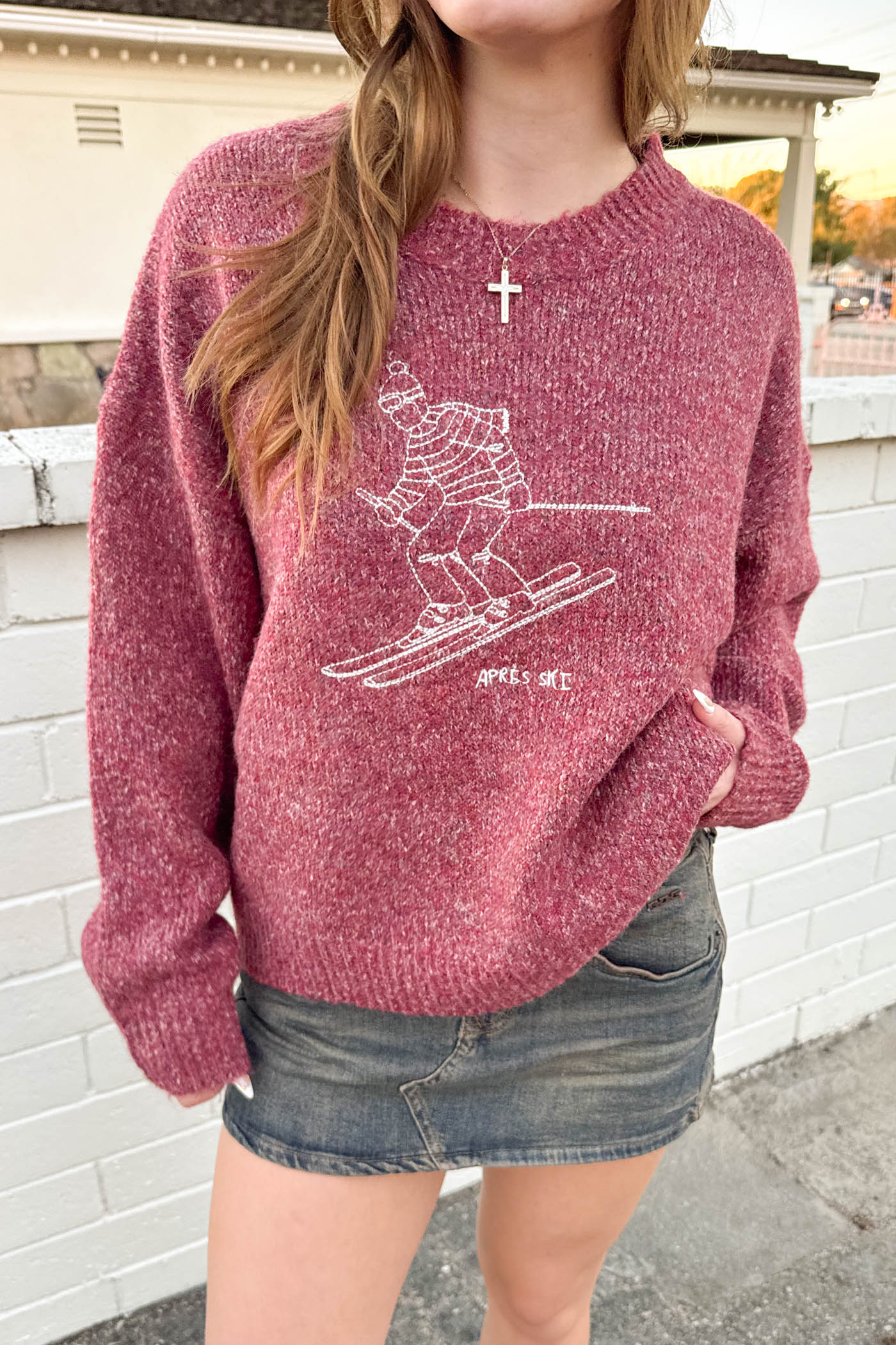 Person wearing a maroon sweater with a white graphic design outdoors.