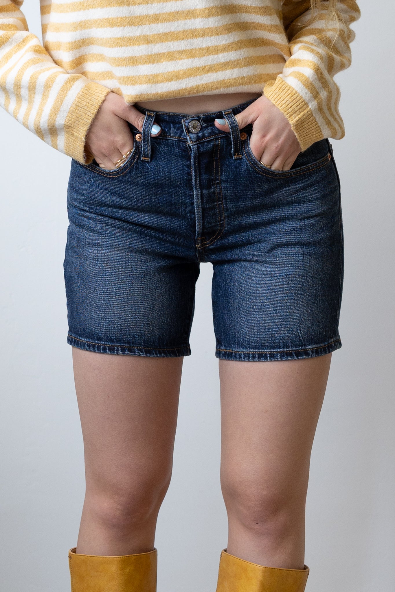 Person wearing a yellow and white striped sweater, blue jeans, and yellow boots on a plain background