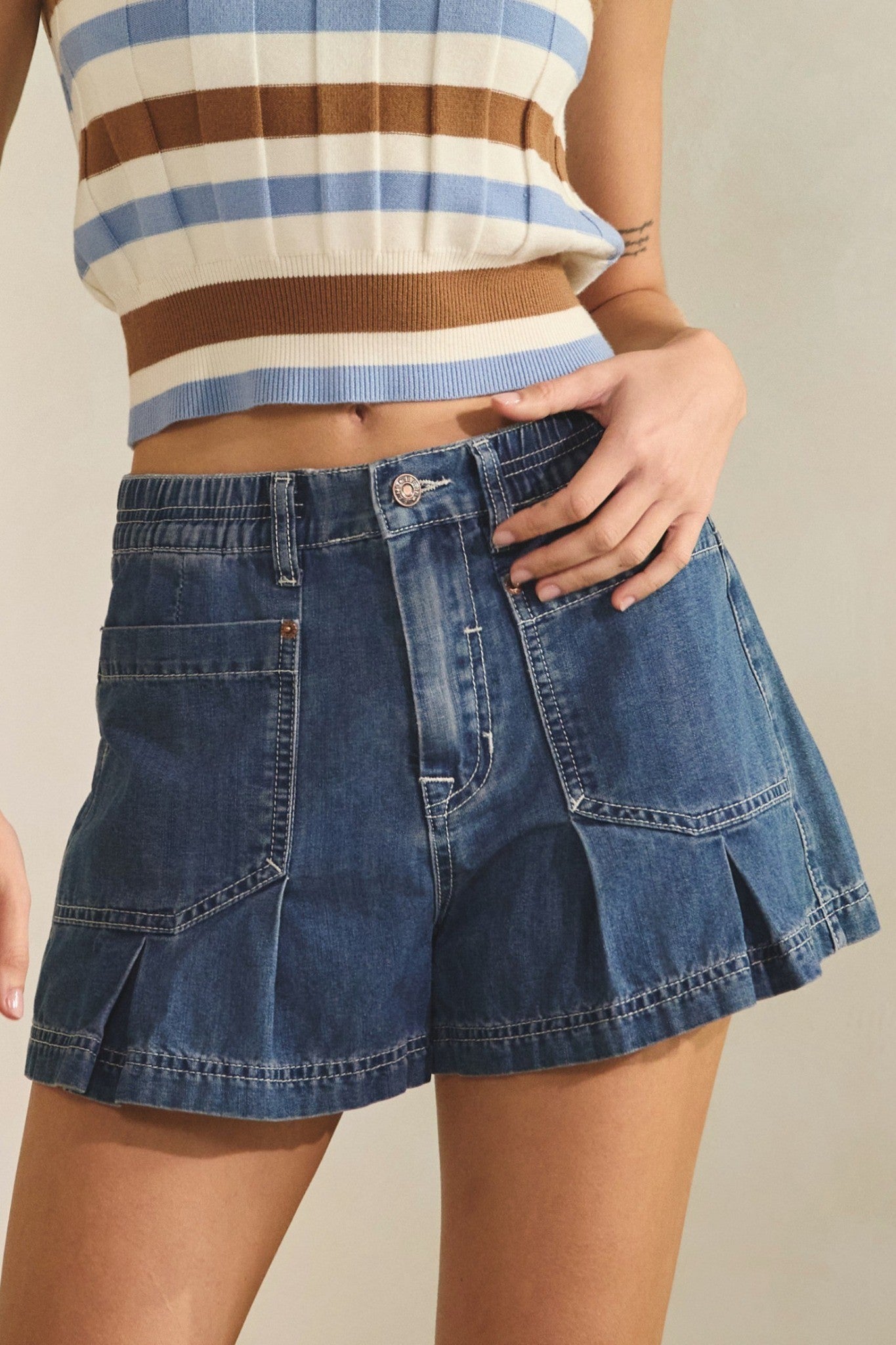 Person wearing a striped sleeveless top and denim shorts on a neutral background