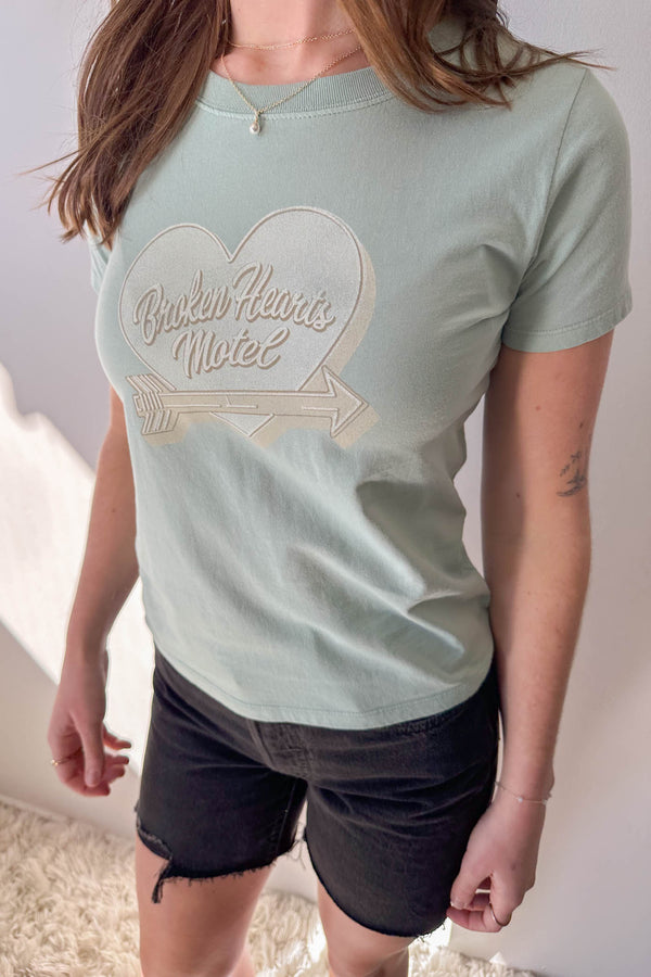 Person wearing a light green t-shirt with a heart-shaped logo and text.