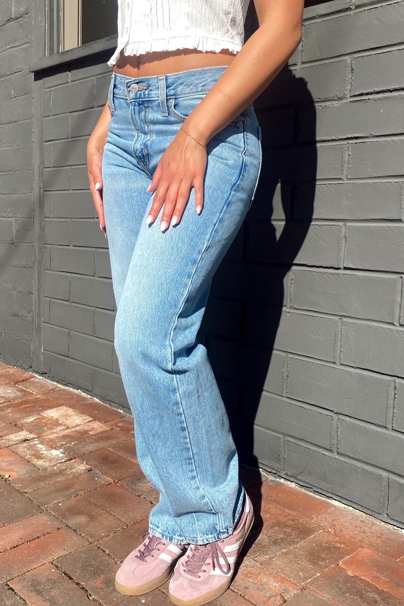 Person wearing light blue jeans and a white top against a gray brick wall.