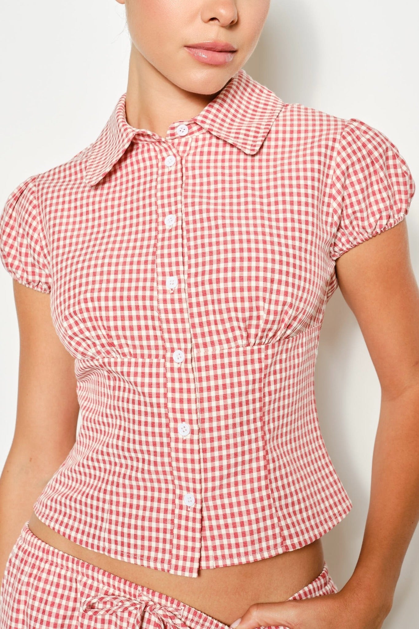 Red and white checkered short-sleeve top worn by a person on a plain background