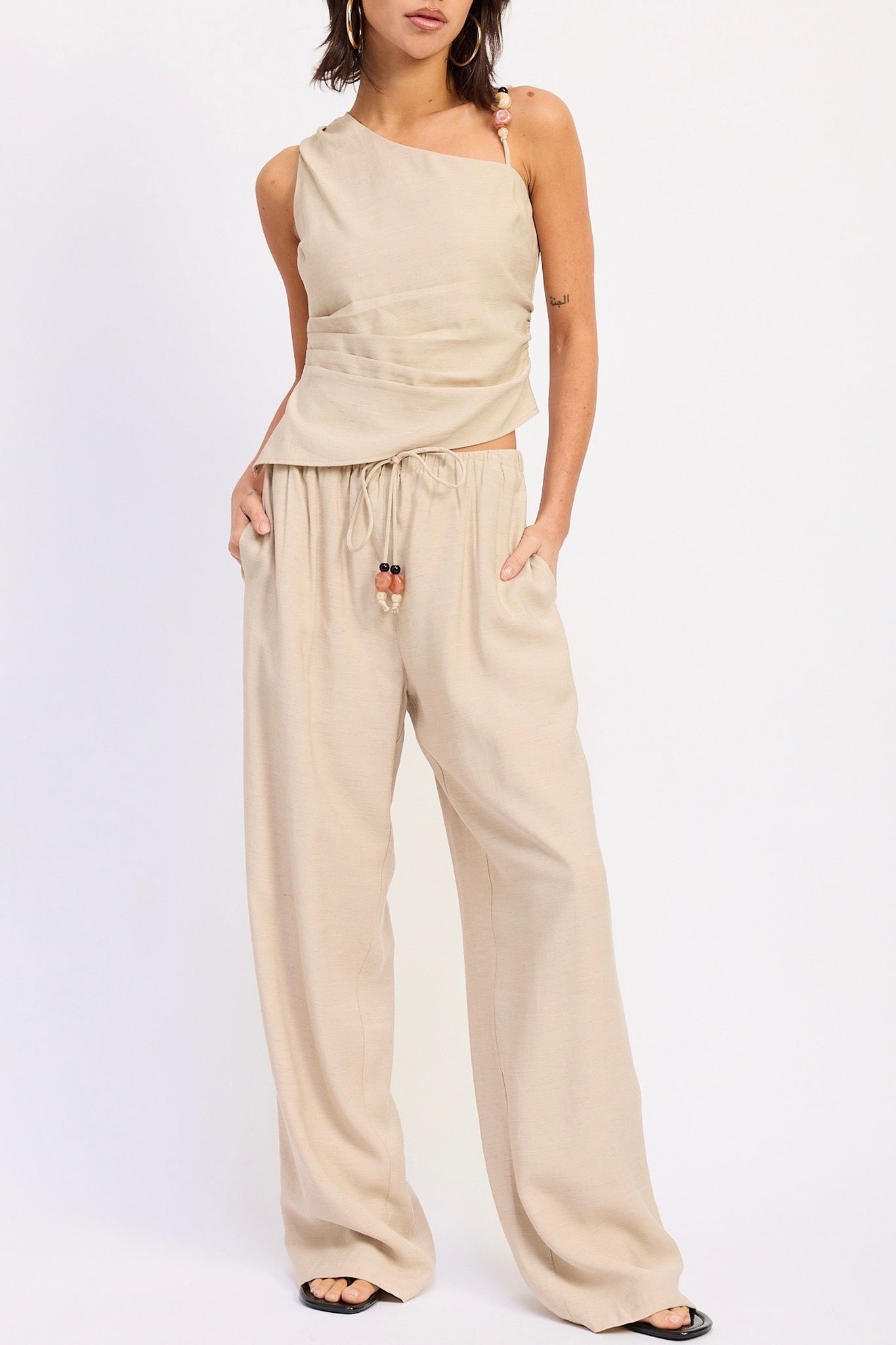Woman wearing a beige one-shoulder top and wide-leg pants on a white background