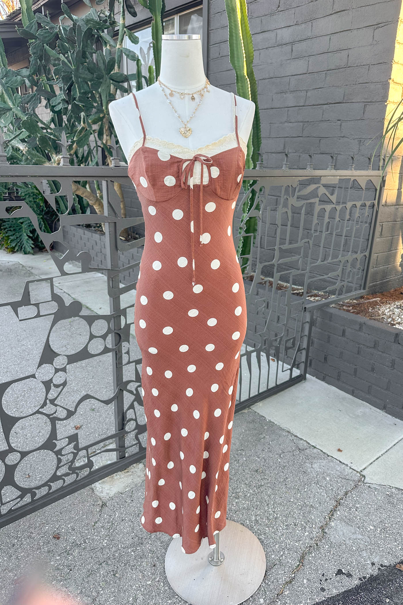 Mannequin wearing a Brown Polka Dotted Maxi Dress standing in front of a fence.
