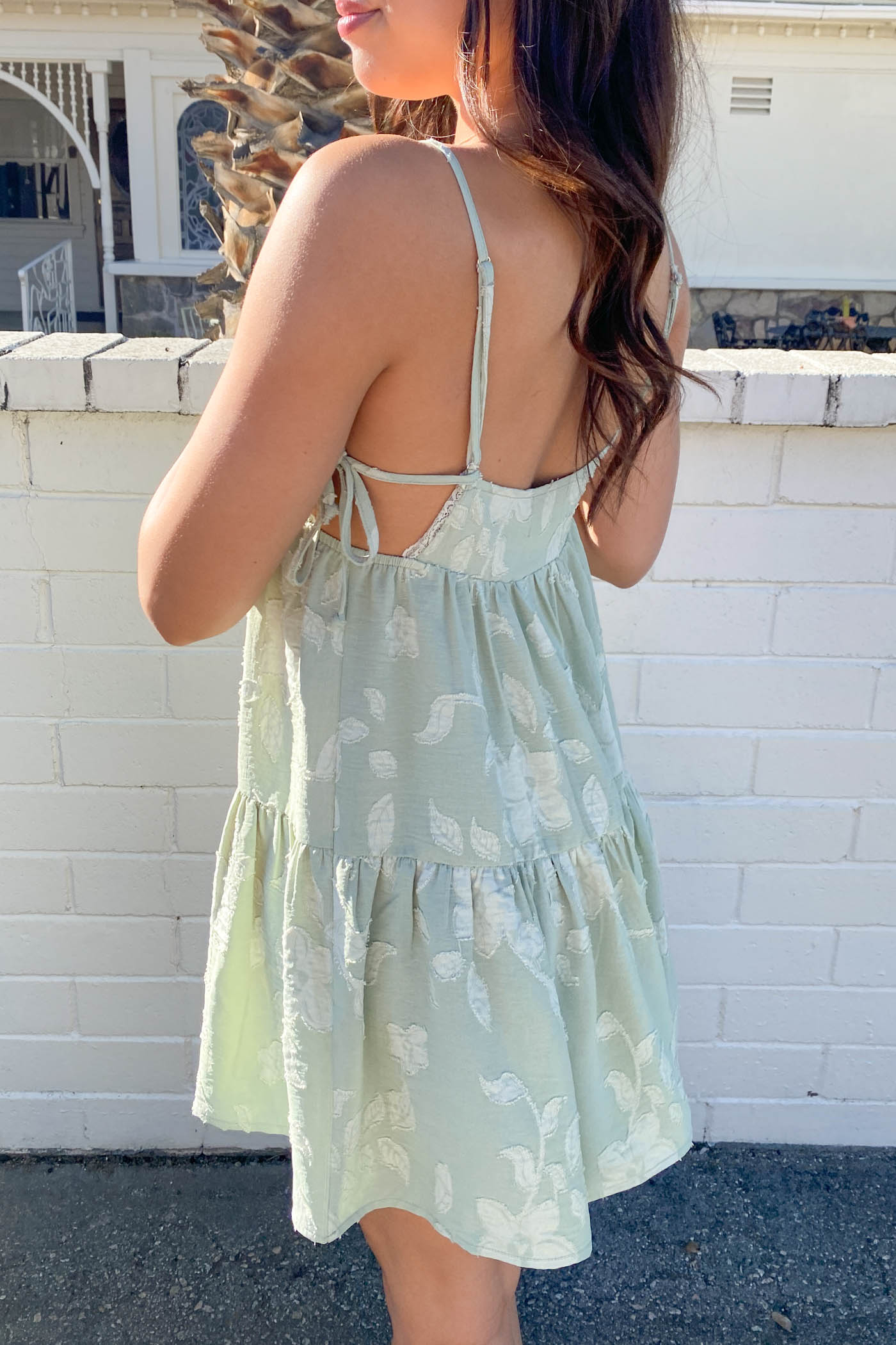 Woman wearing a light green floral dress with a white brick wall background
