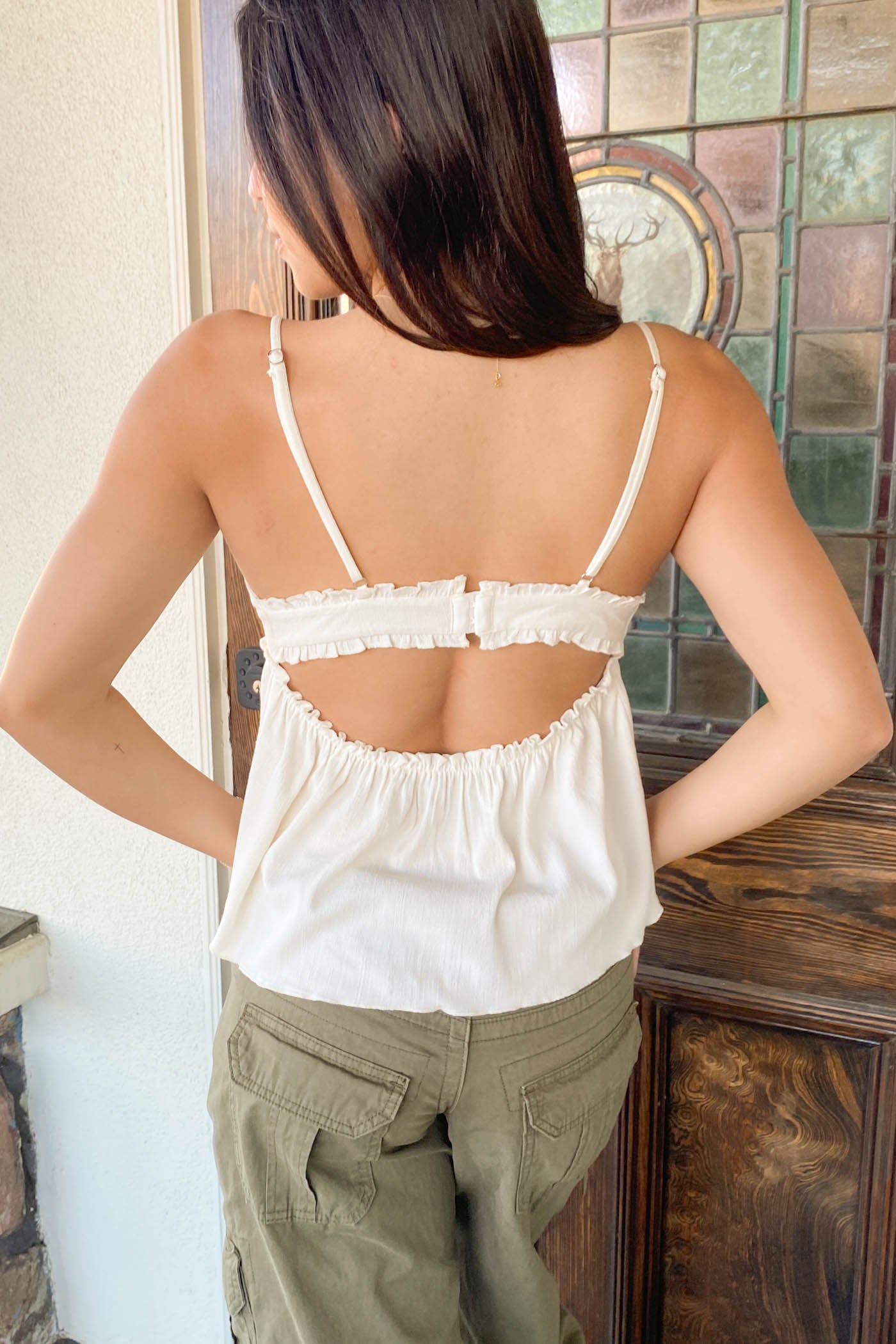Person wearing a white lace top and green pants in front of a stained glass window.