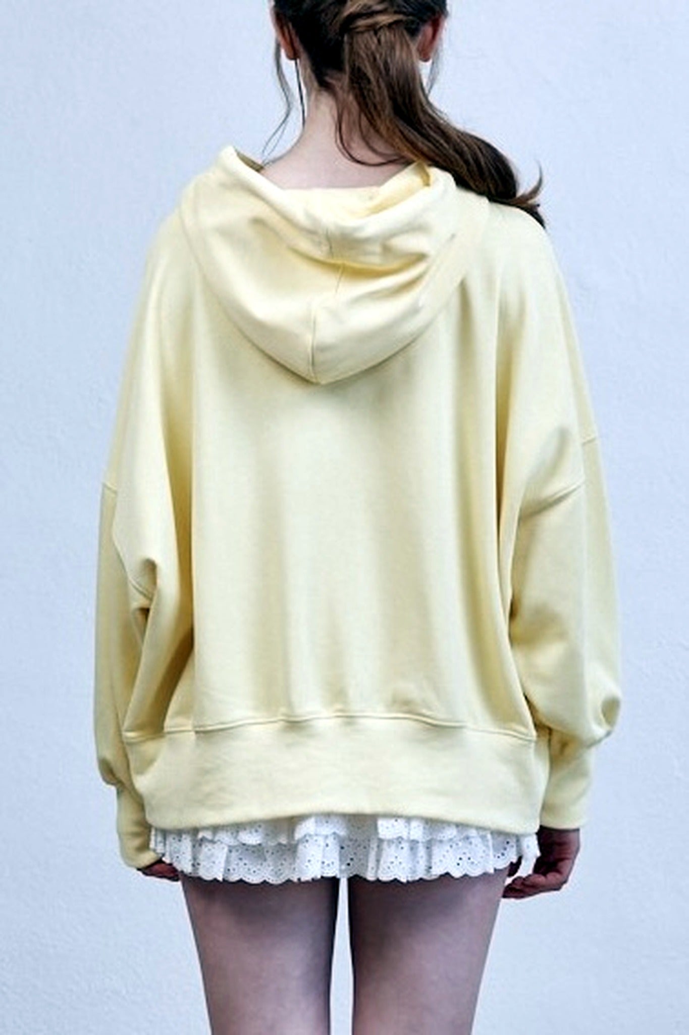 Person wearing a light yellow hoodie and white lace shorts on a plain background