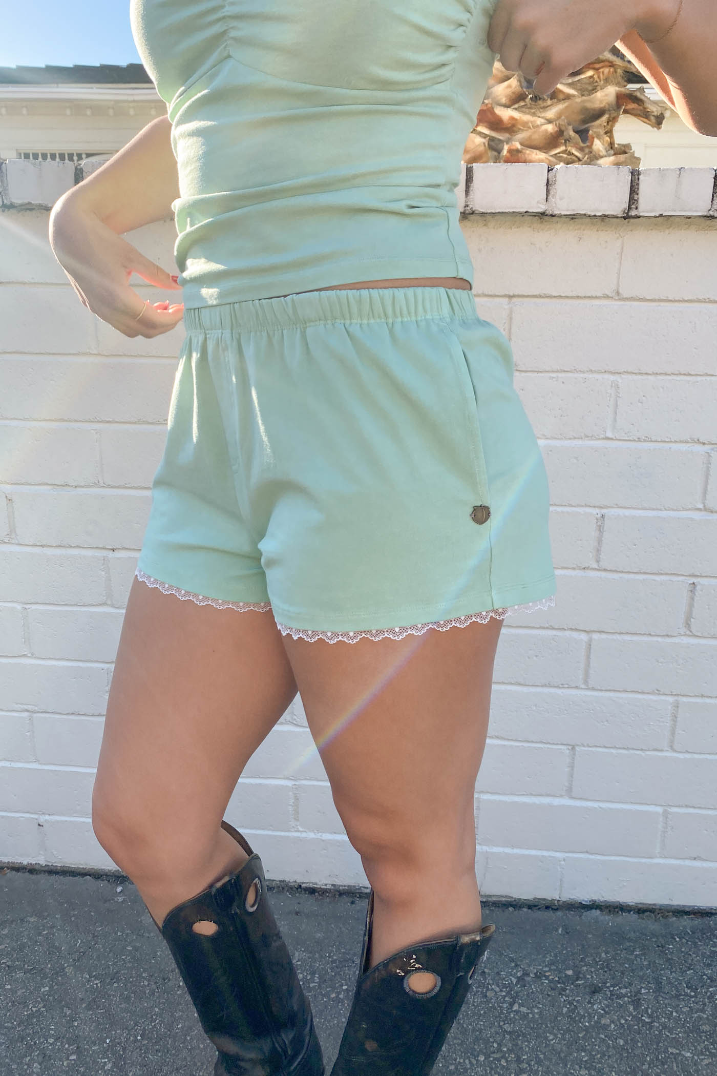 Person wearing a light green outfit with lace trim against a white brick wall.