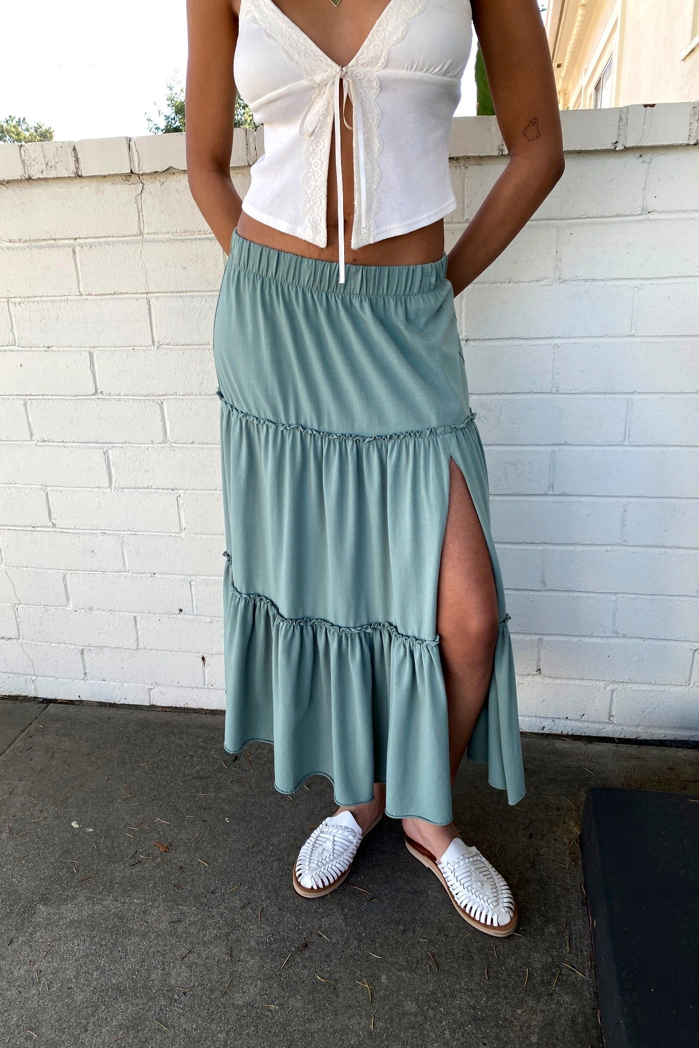 Person wearing a white top and green skirt with a white brick wall background