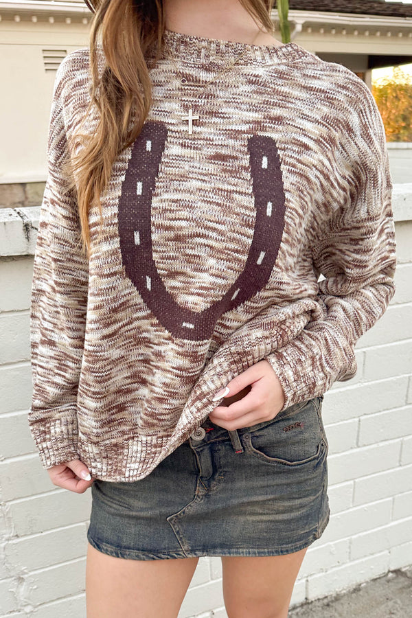 Person wearing a sweater with a horseshoe design against a white brick wall.