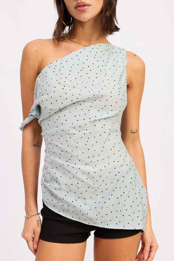 Woman wearing a light blue one-shoulder top with black polka dots on a white background