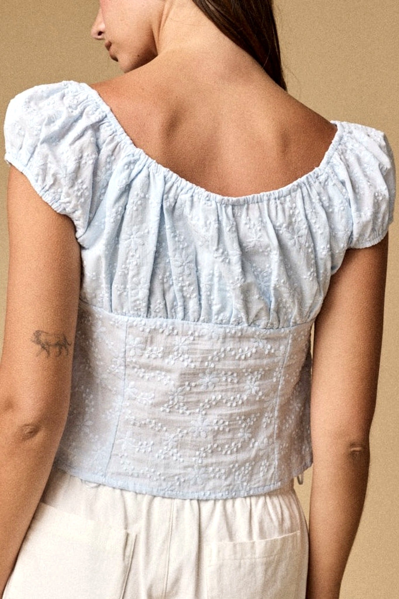 Light blue top with ruffled shoulders worn by a person on a beige background