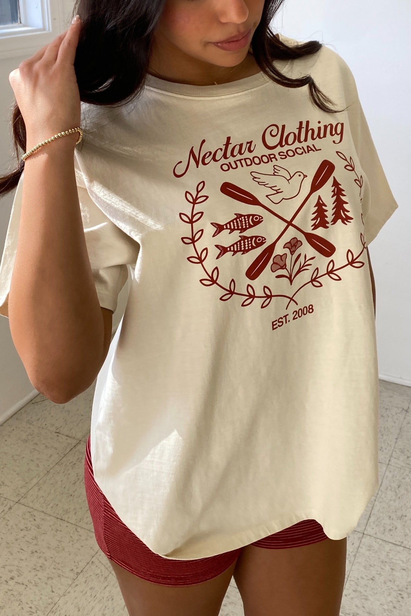 Person wearing a cream t-shirt with red graphics and text, standing indoors.