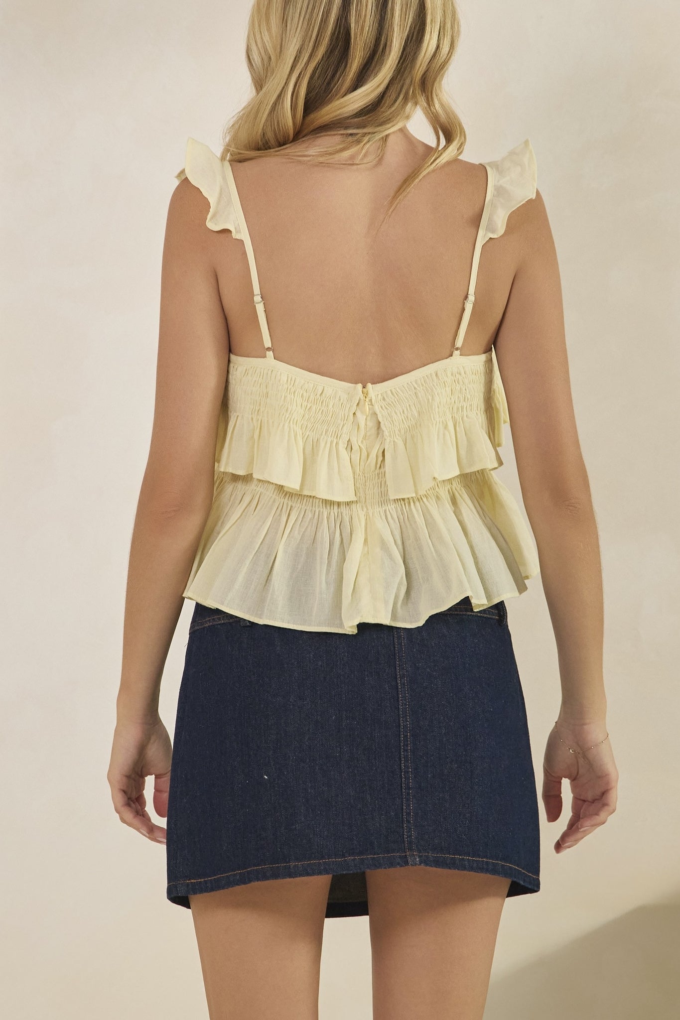 Woman wearing a yellow ruffled top and denim skirt on a beige background