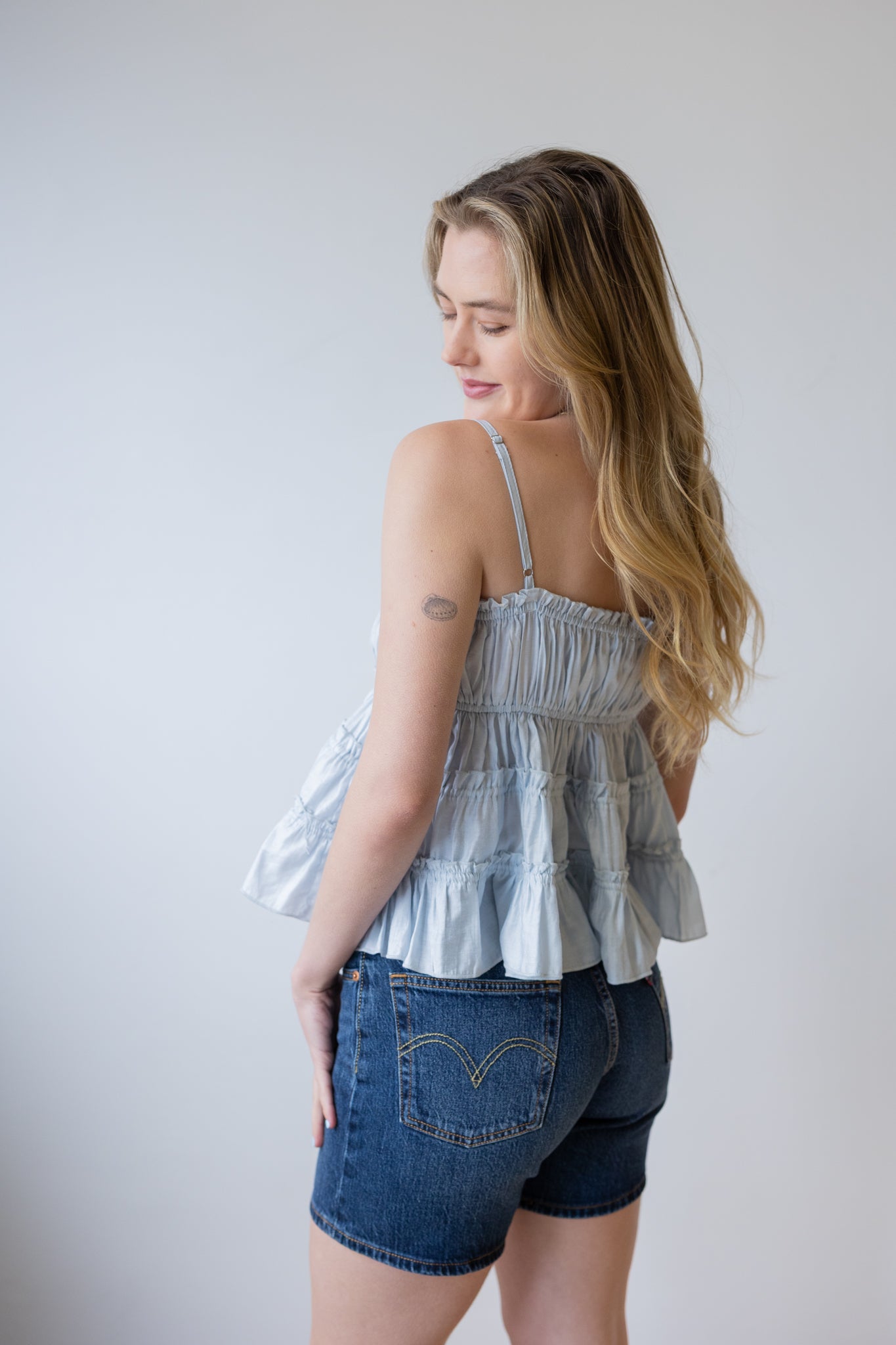 Woman wearing a layered top and denim shorts against a plain background