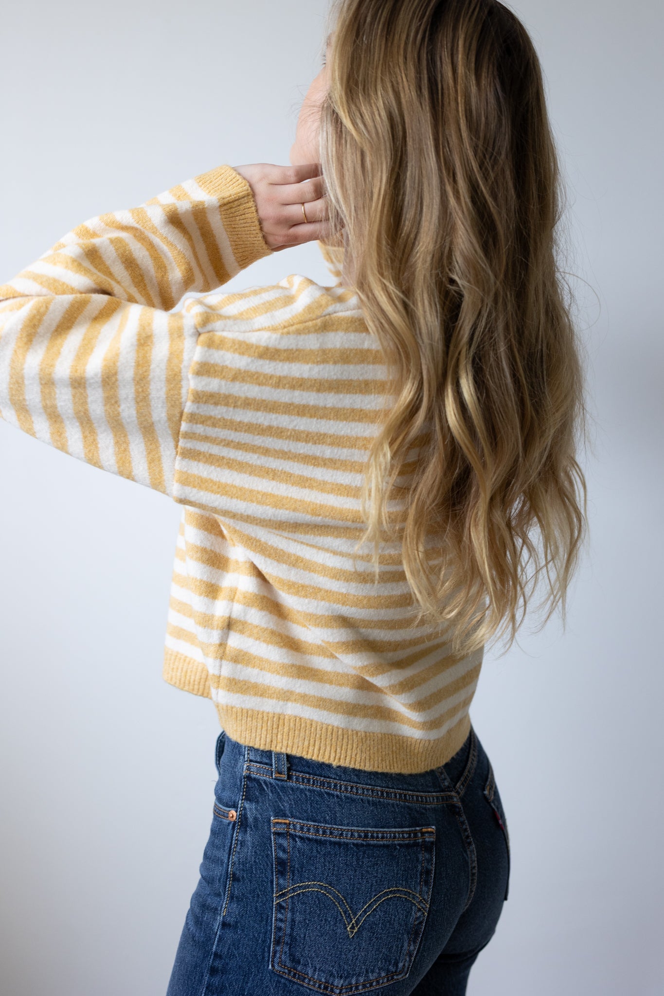 Person wearing a yellow and white striped sweater and blue jeans against a plain background
