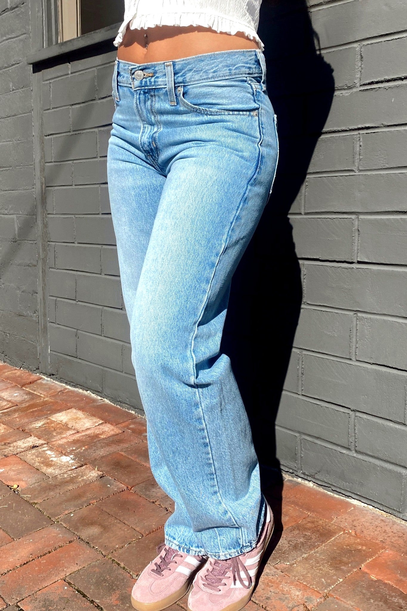 Person wearing light blue jeans and pink shoes against a gray brick wall.