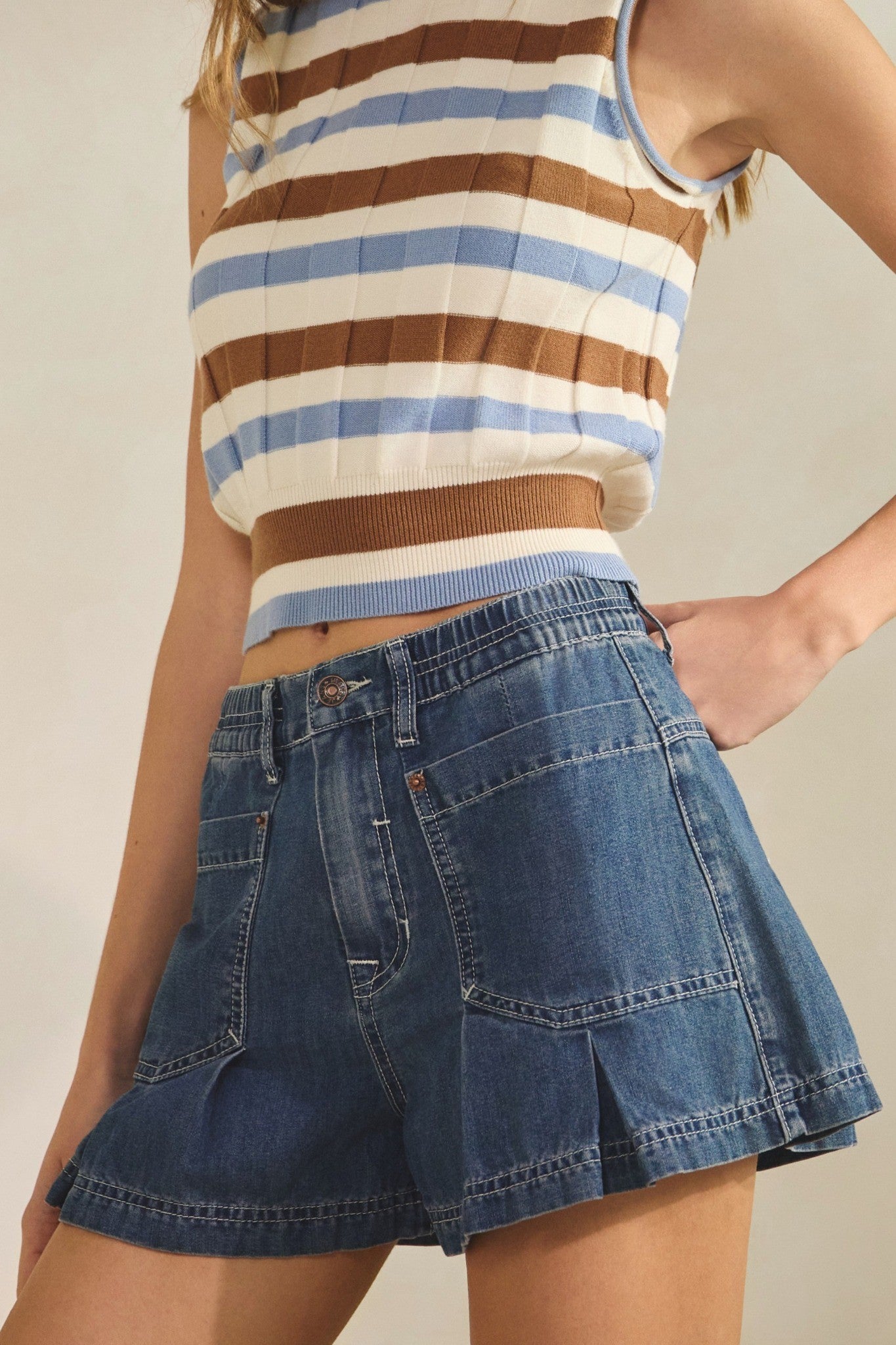 Person wearing a striped tank top and denim skirt on a neutral background