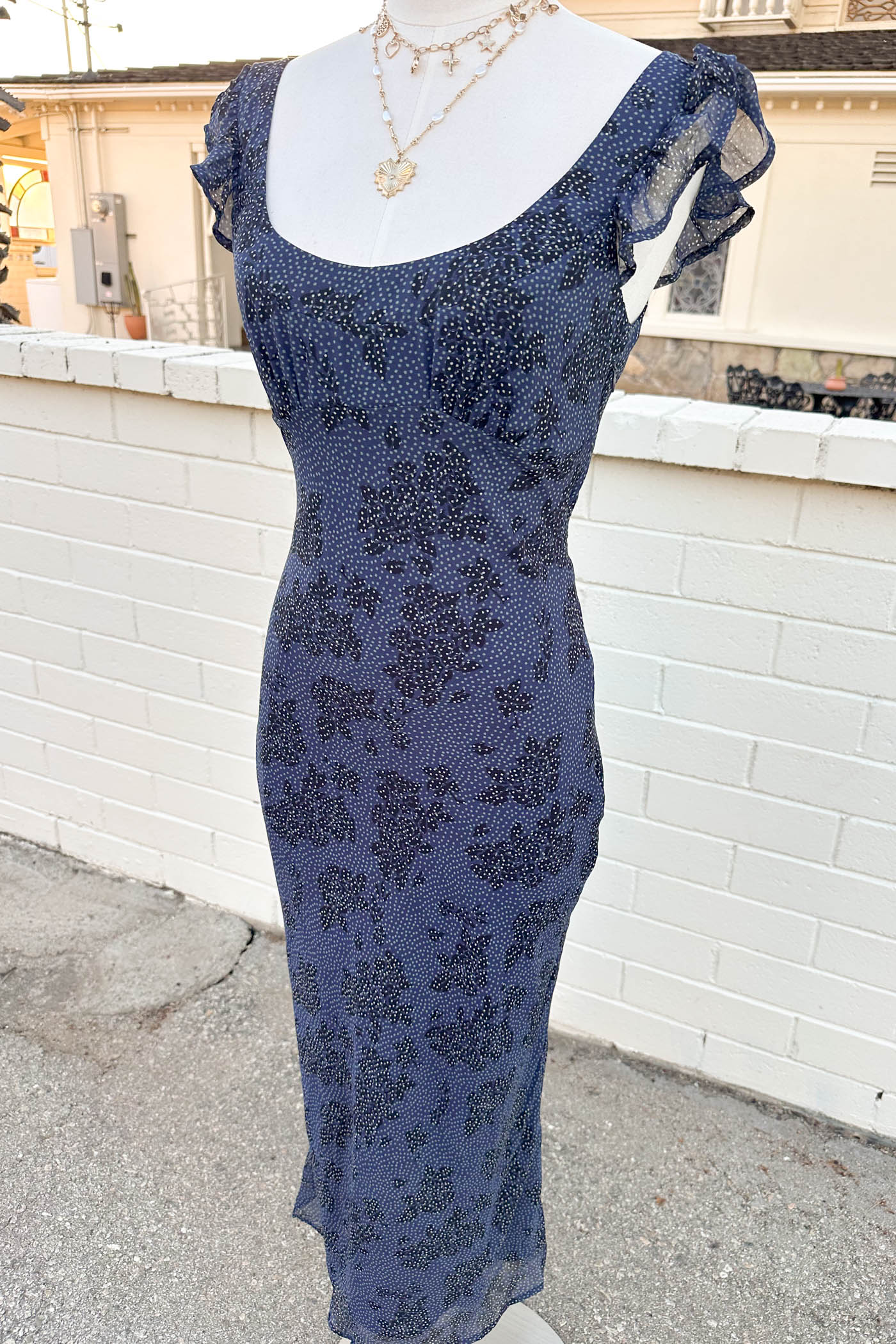 Blue floral dress on a mannequin against a white brick wall.