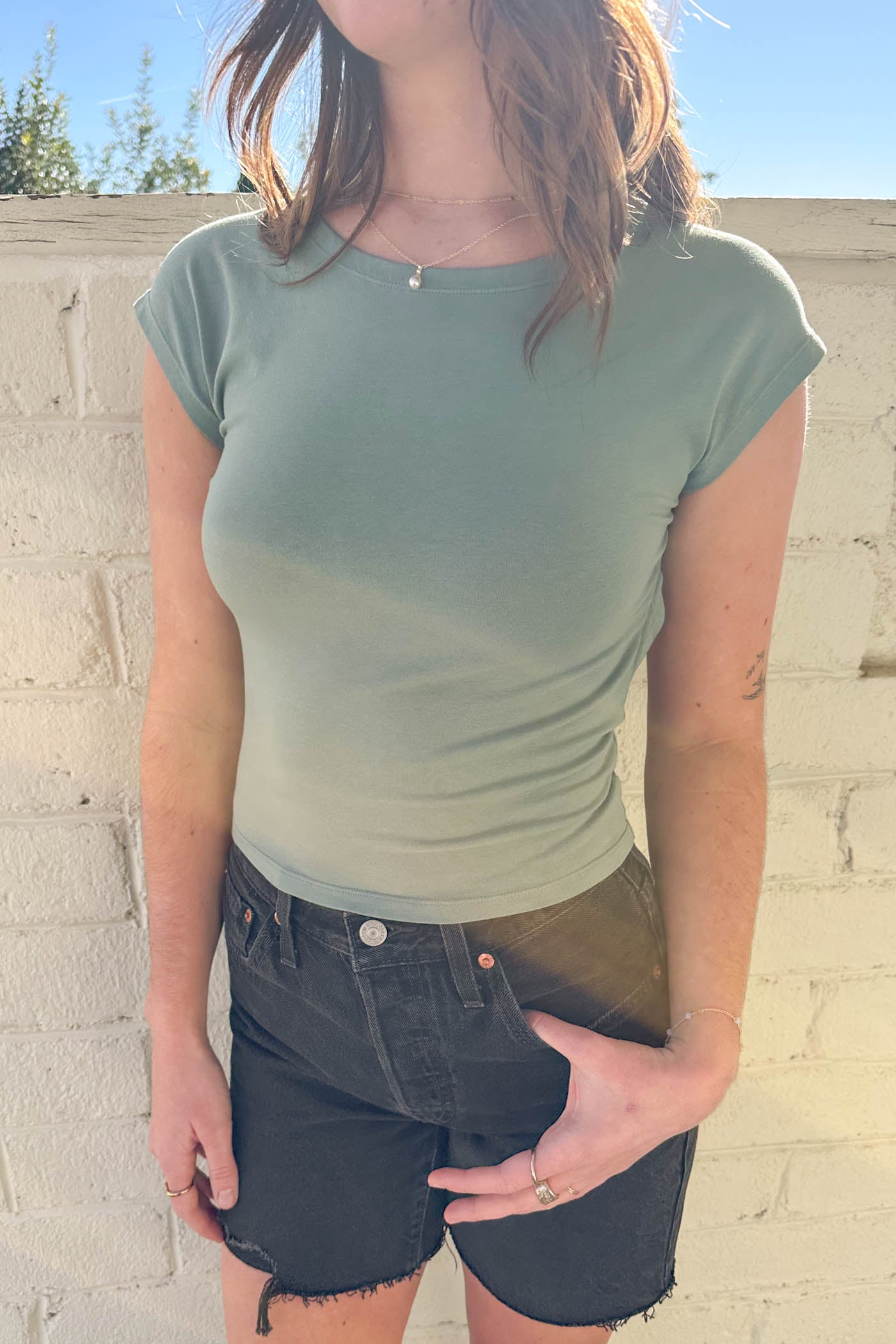 Person wearing a green ombre t-shirt and black shorts against a light-colored wall.
