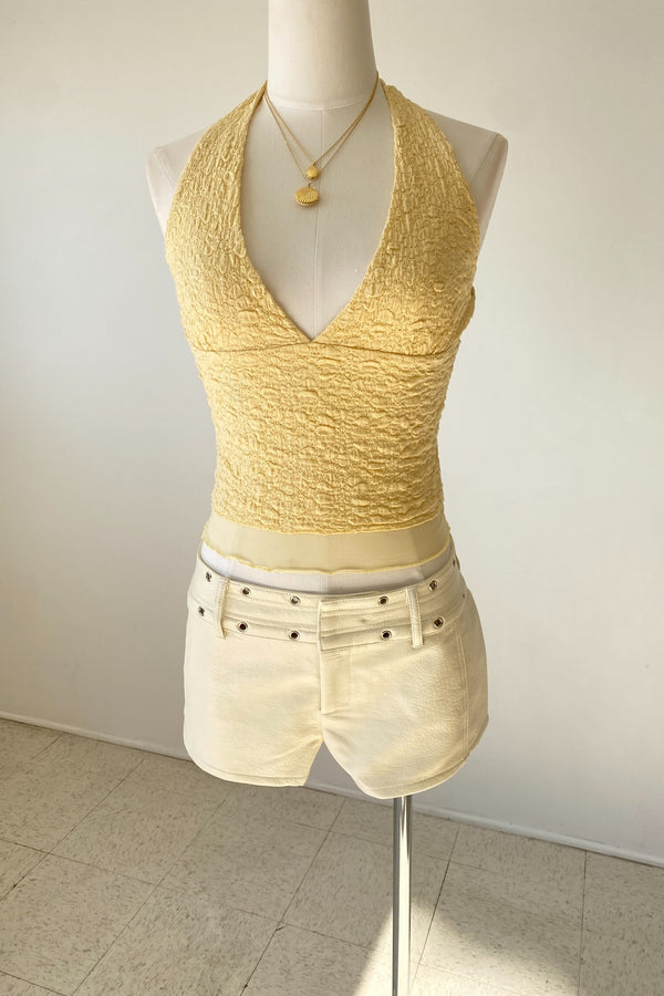 Mannequin wearing a yellow sleeveless top and white shorts on a plain background