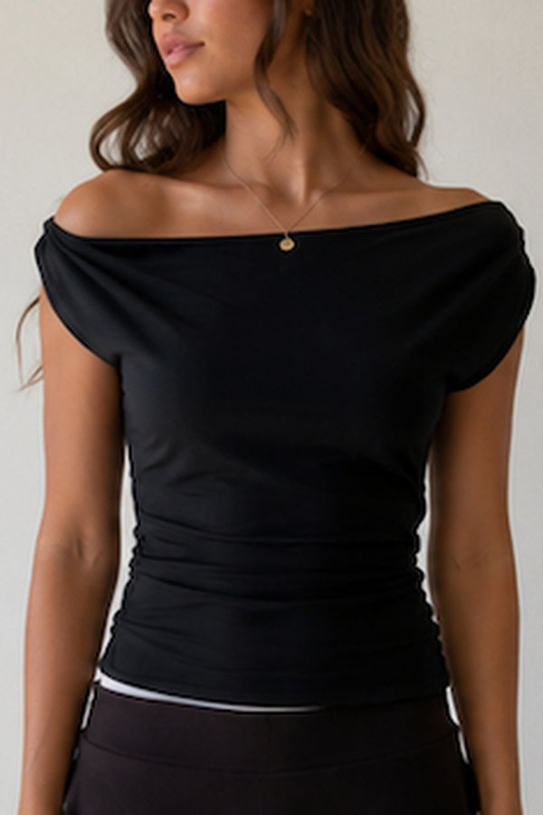 A woman wearing a black off-the-shoulder ruched top and cream-colored tiered skirt against a light gray background.