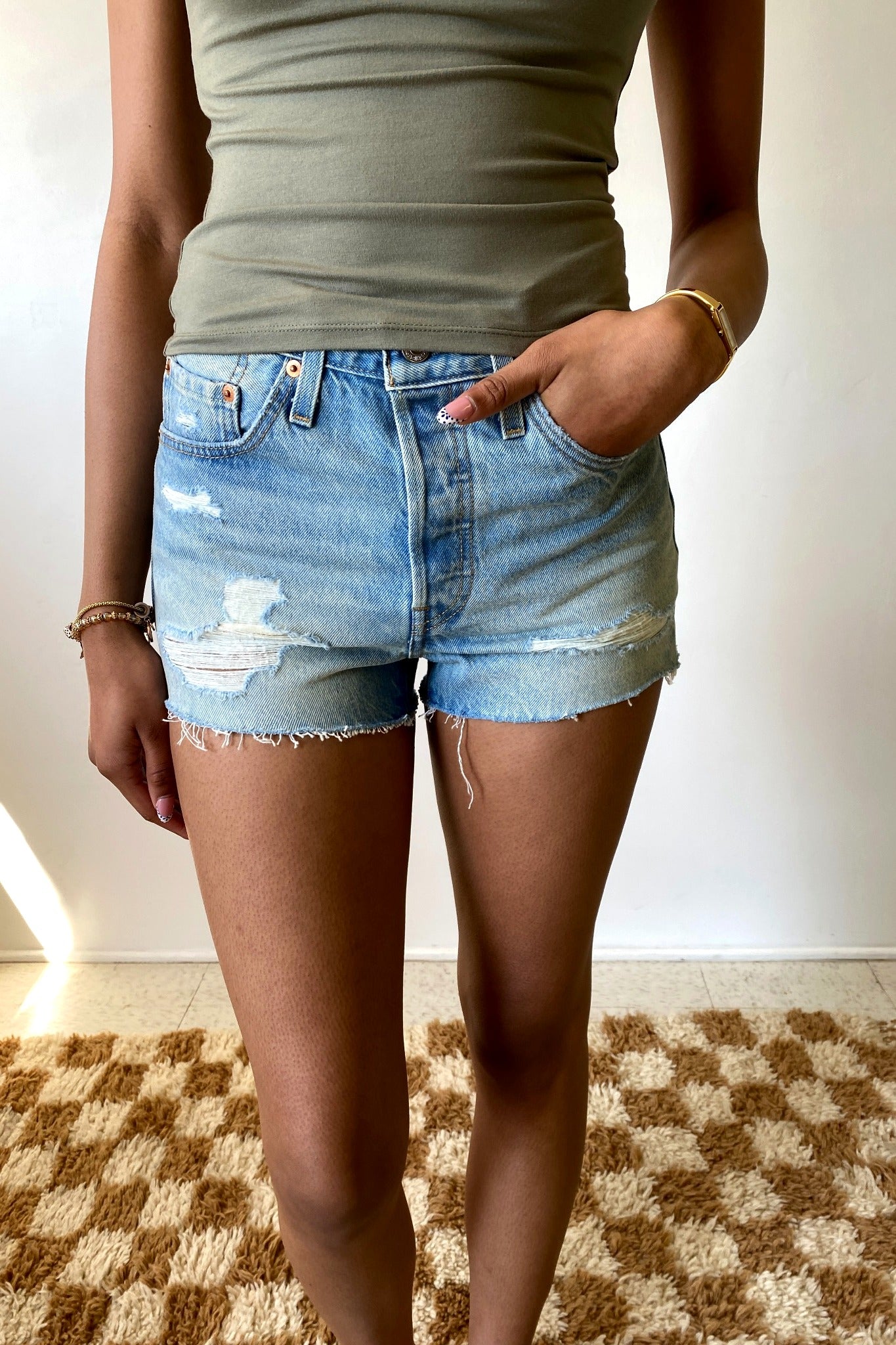 Person wearing a green top and blue denim shorts on a checkered floor.