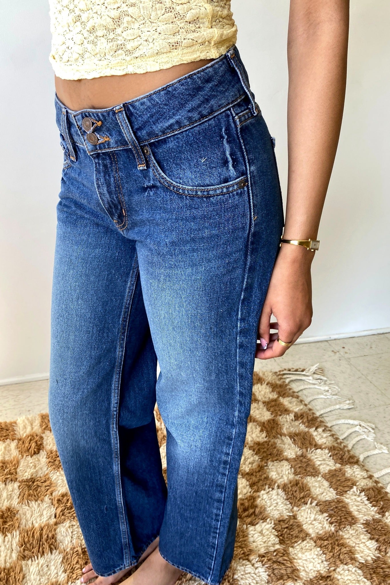 Woman wearing blue jeans standing in front of white wall. 