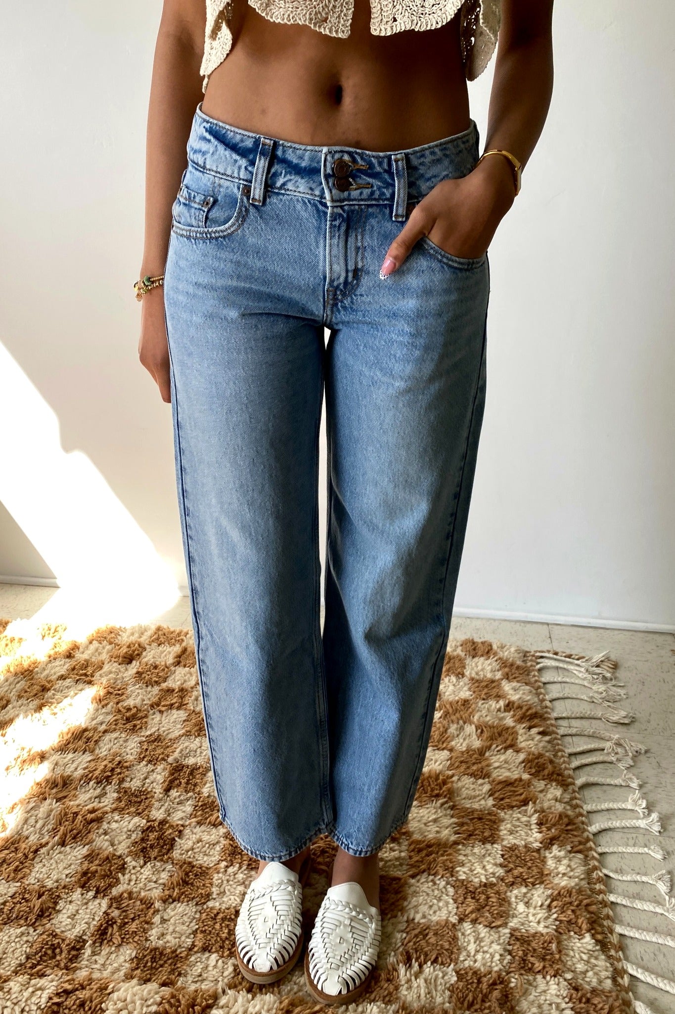 Person wearing blue jeans and a cropped top on a checkered rug.
