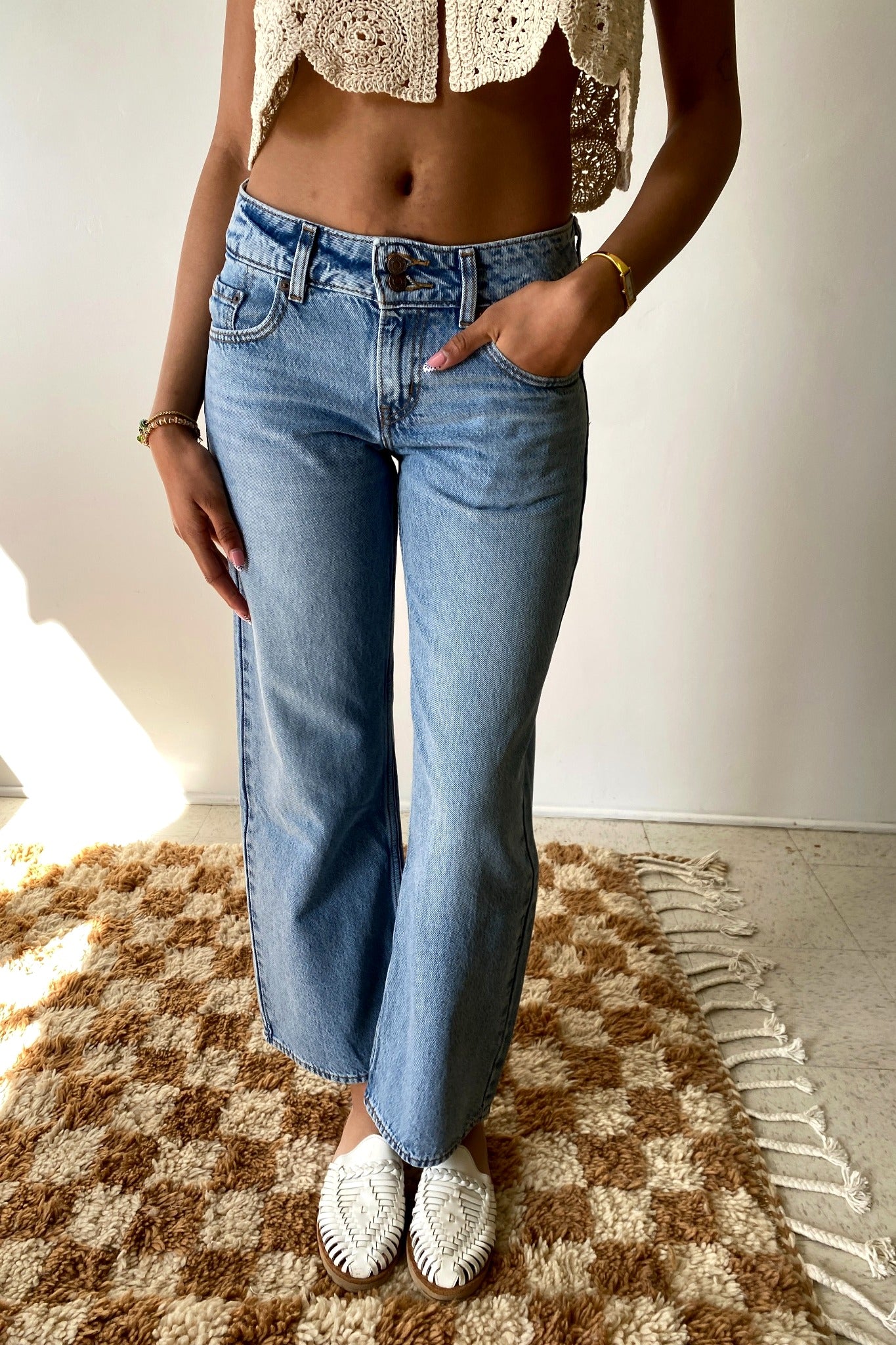 Person wearing blue jeans and a cropped top on a checkered rug.
