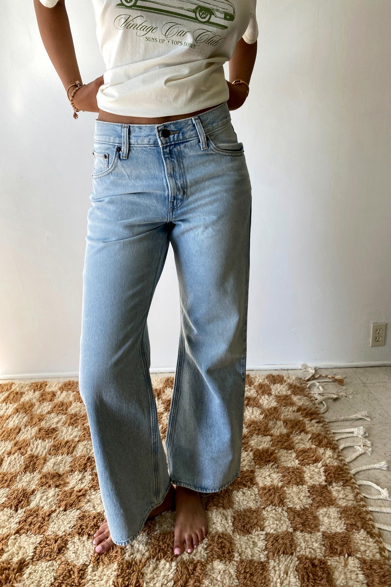 Person wearing a graphic t-shirt and light blue jeans standing on a checkered rug.