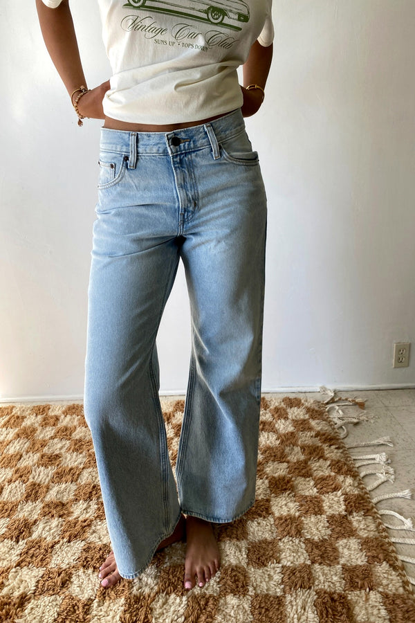 Person wearing a graphic t-shirt and light blue jeans standing on a checkered rug.