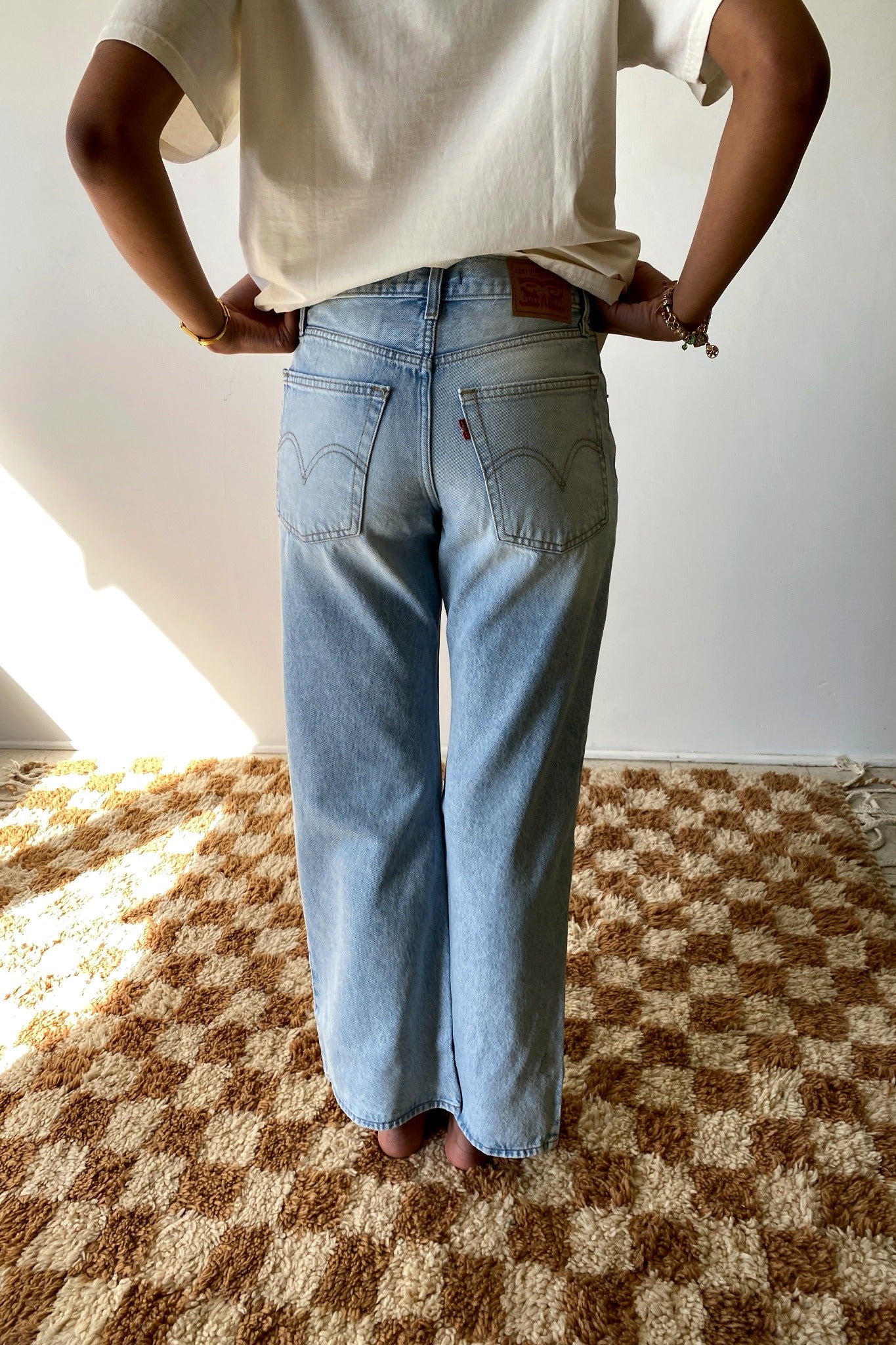 Person wearing light blue jeans and a white t-shirt on a checkered floor.