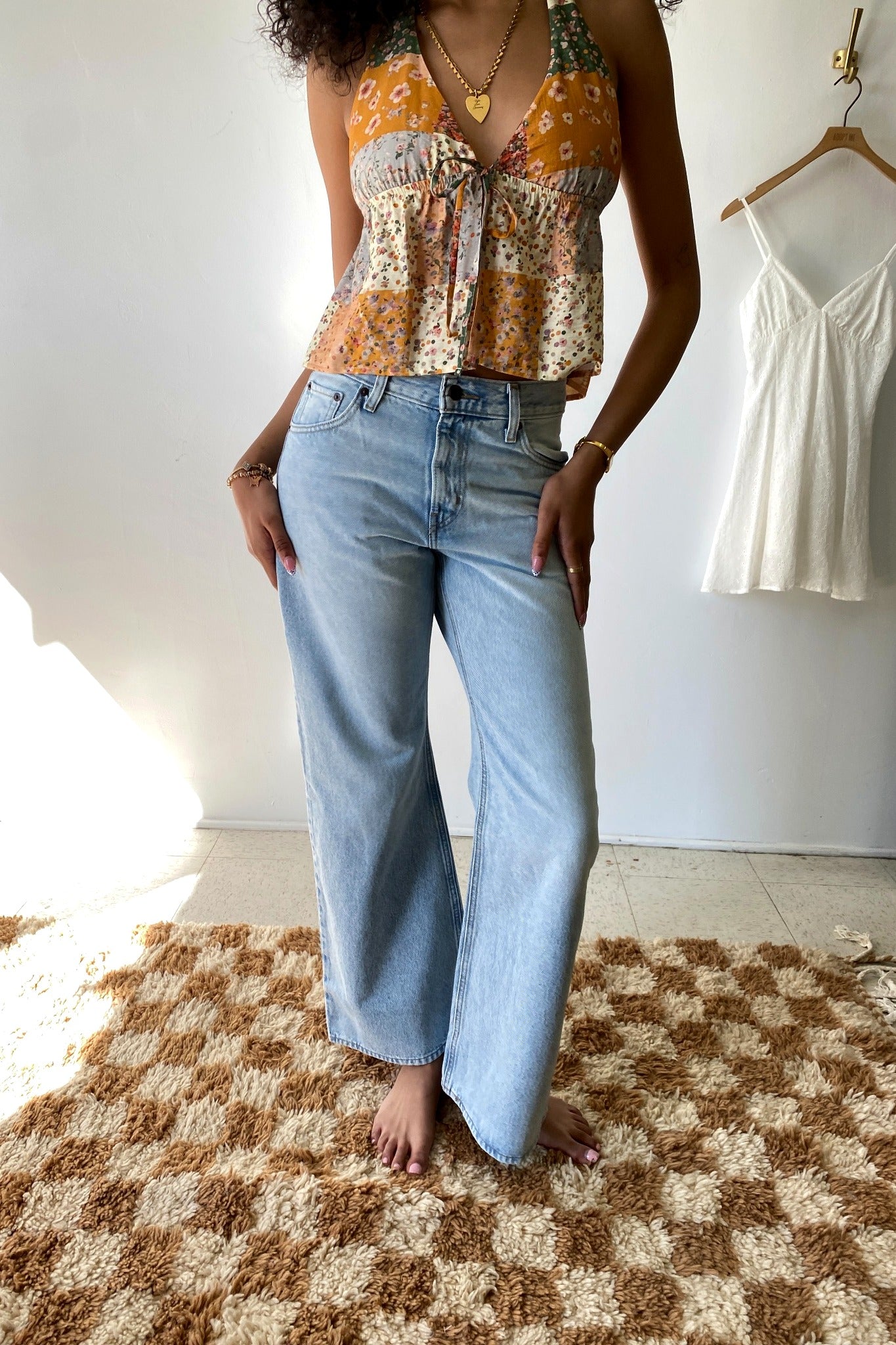 Person wearing a floral shirt and light blue jeans standing on a checkered rug.