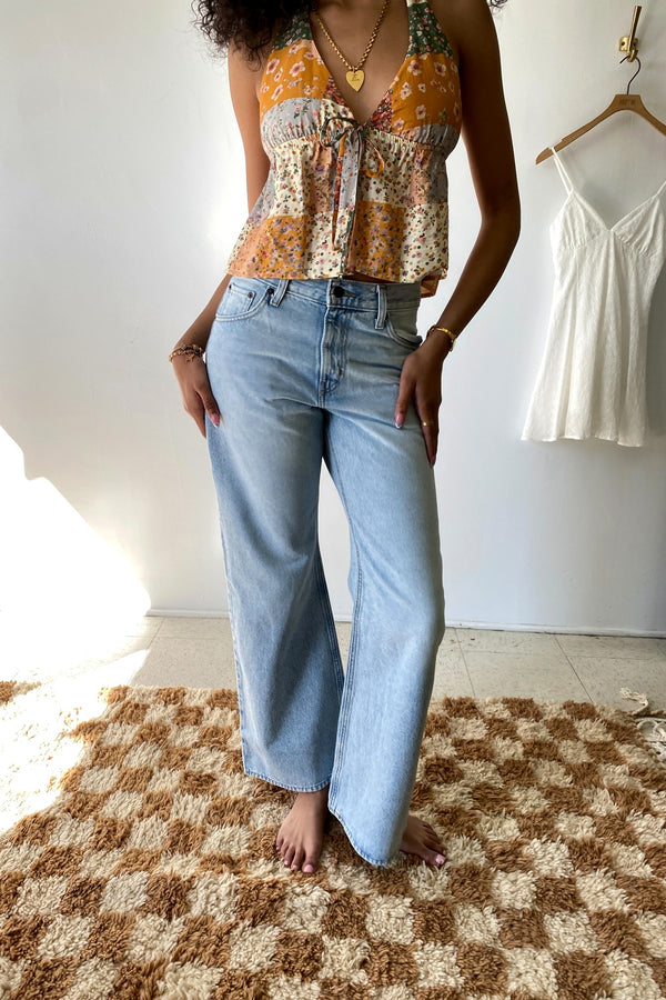 Person wearing a floral shirt and light blue jeans standing on a checkered rug.