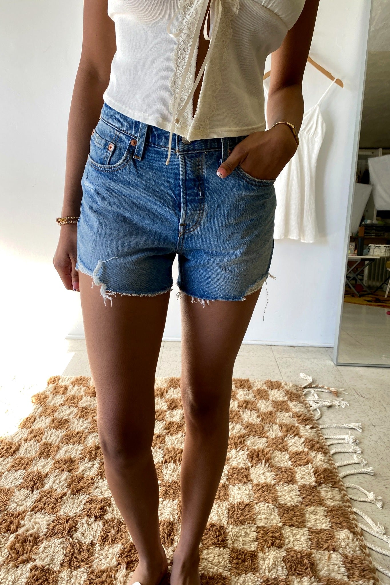 Person wearing denim shorts standing on a checkered rug indoors.