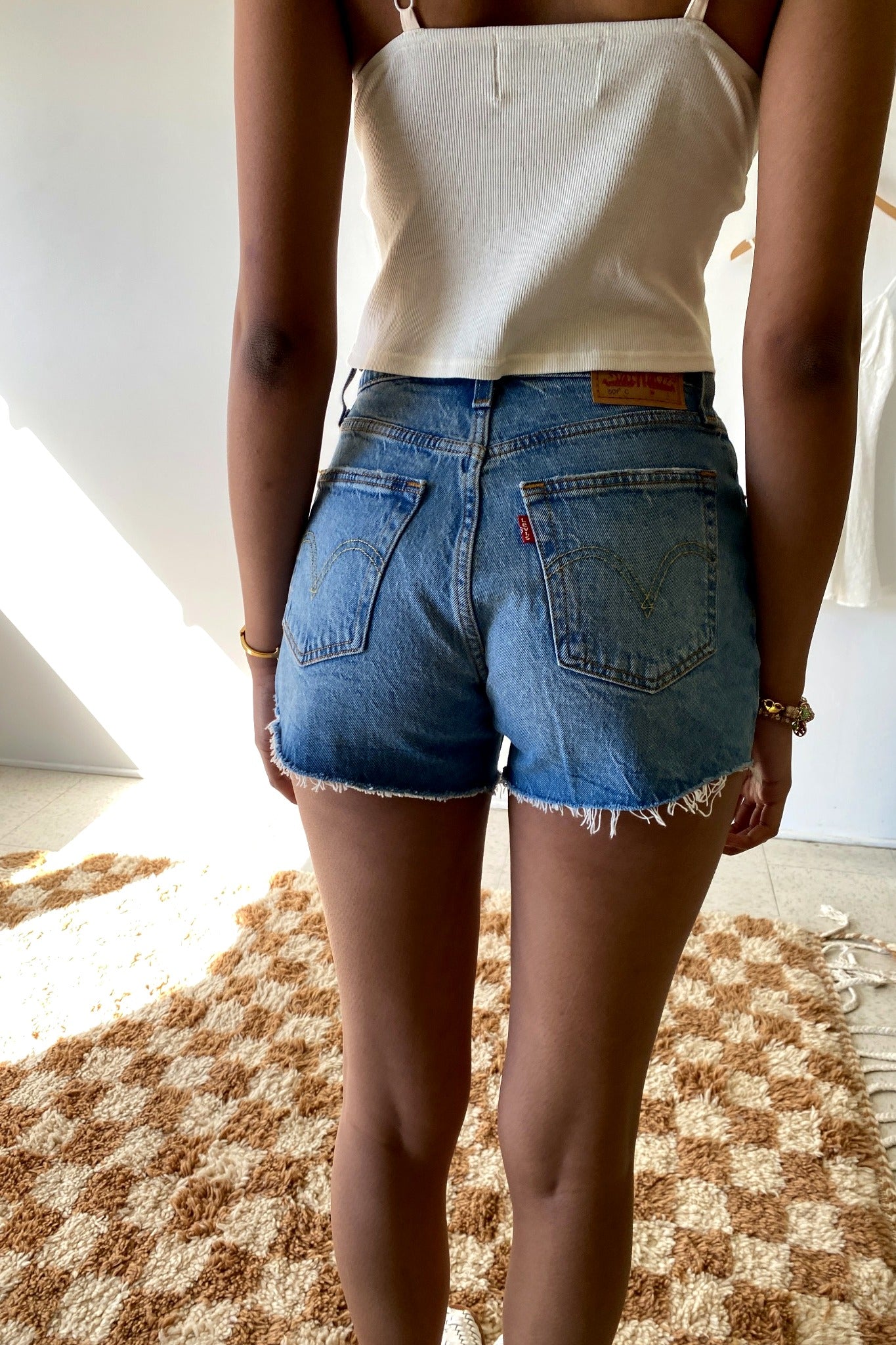 Person wearing a white tank top and blue denim shorts indoors.
