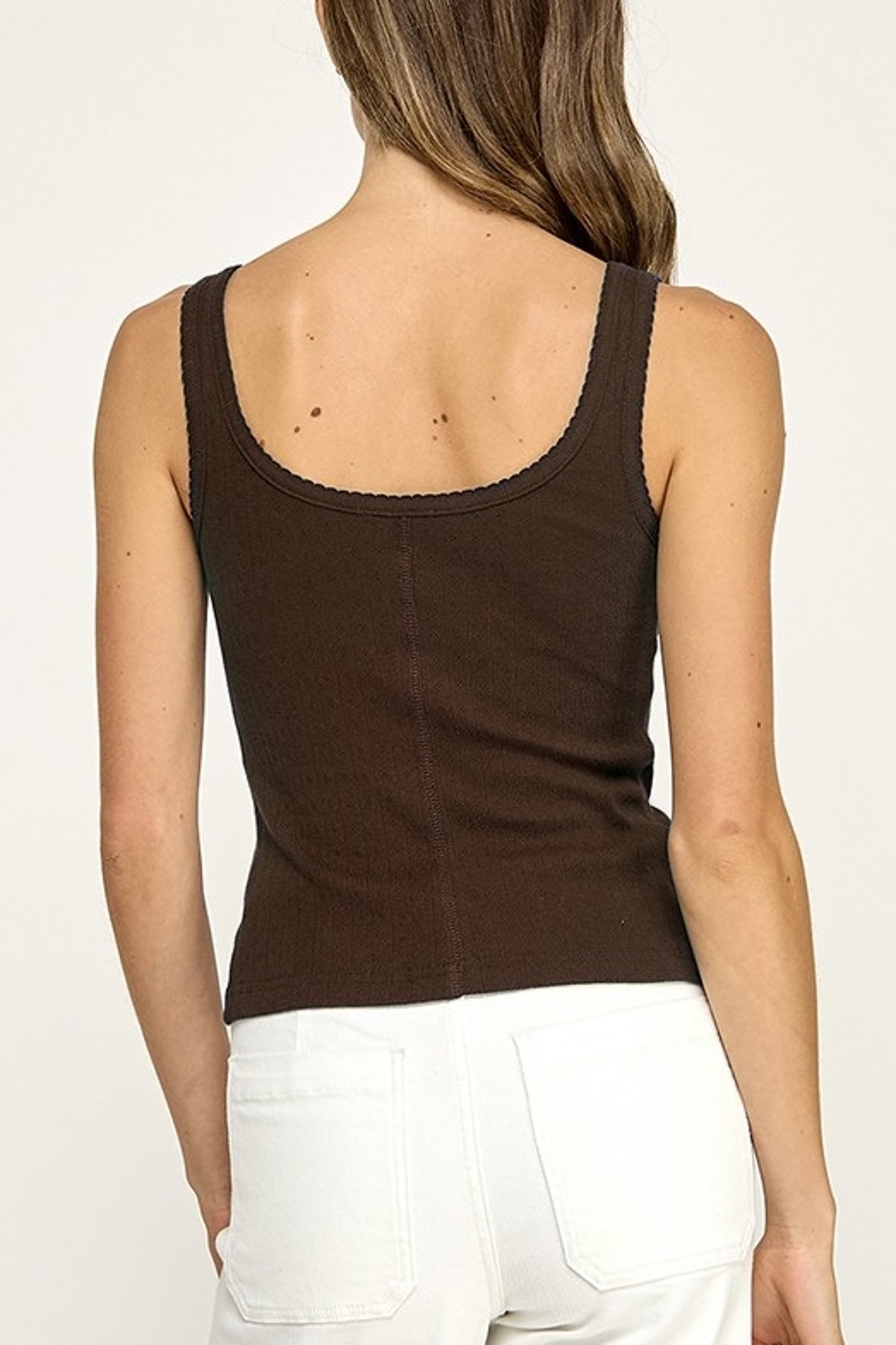 Person wearing a brown tank top and white pants on a plain background