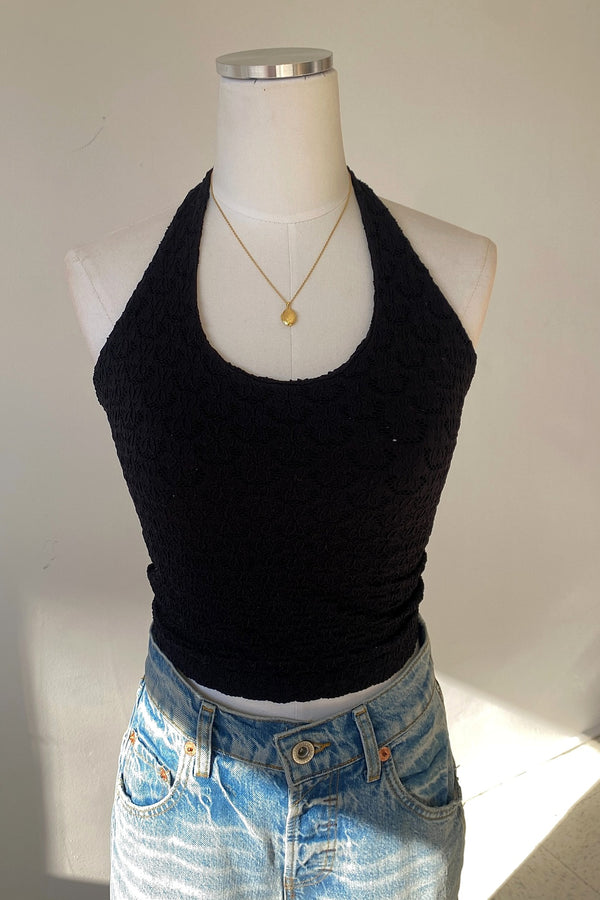 Black halter top on a mannequin with blue jeans and a necklace against a white background