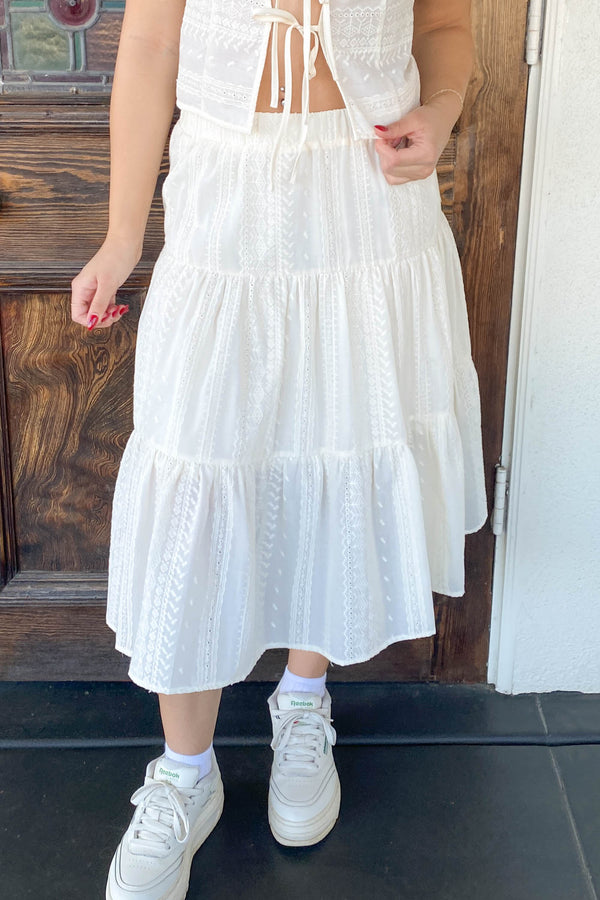 Person wearing a white dress with ruffled layers and white sneakers in front of a wooden door.