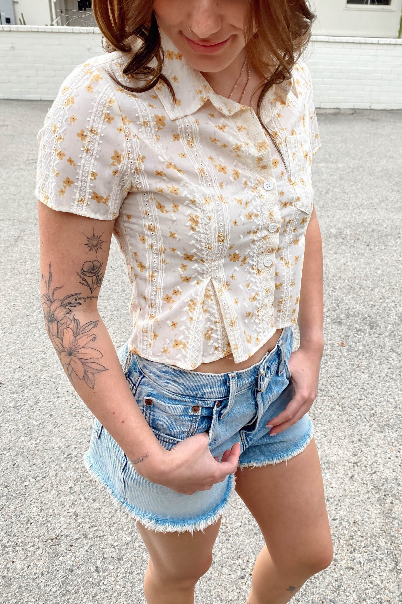 Woman wearing a white floral blouse and denim shorts outdoors.