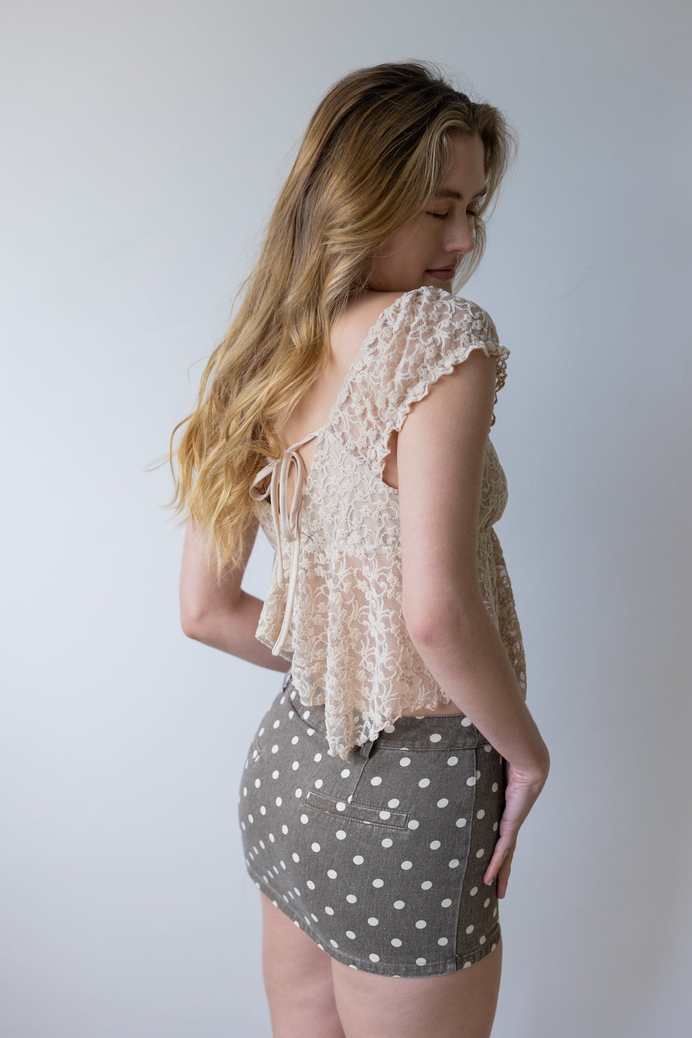 Woman wearing a beige lace top and polka dot skirt against a plain background