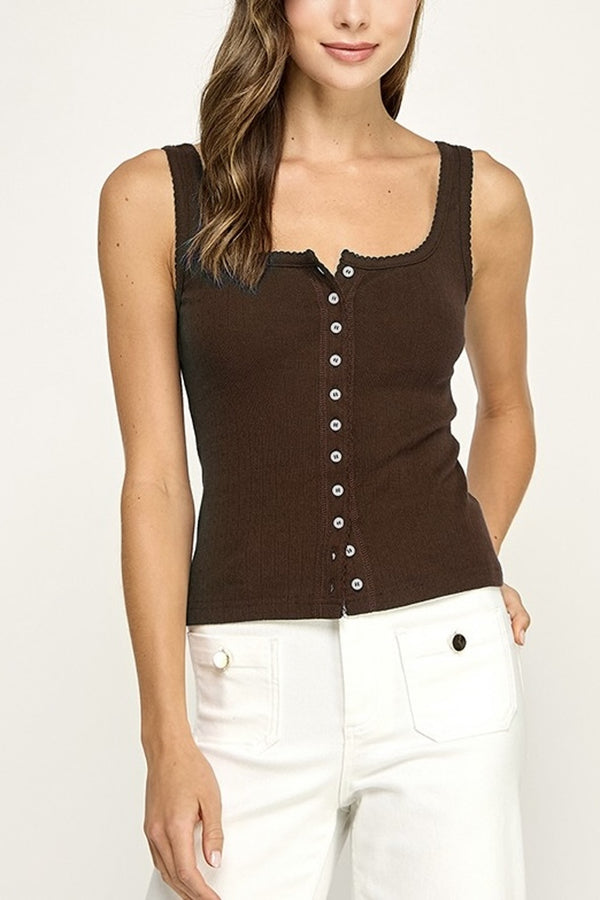 Woman wearing a brown button-up tank top and white pants on a plain background