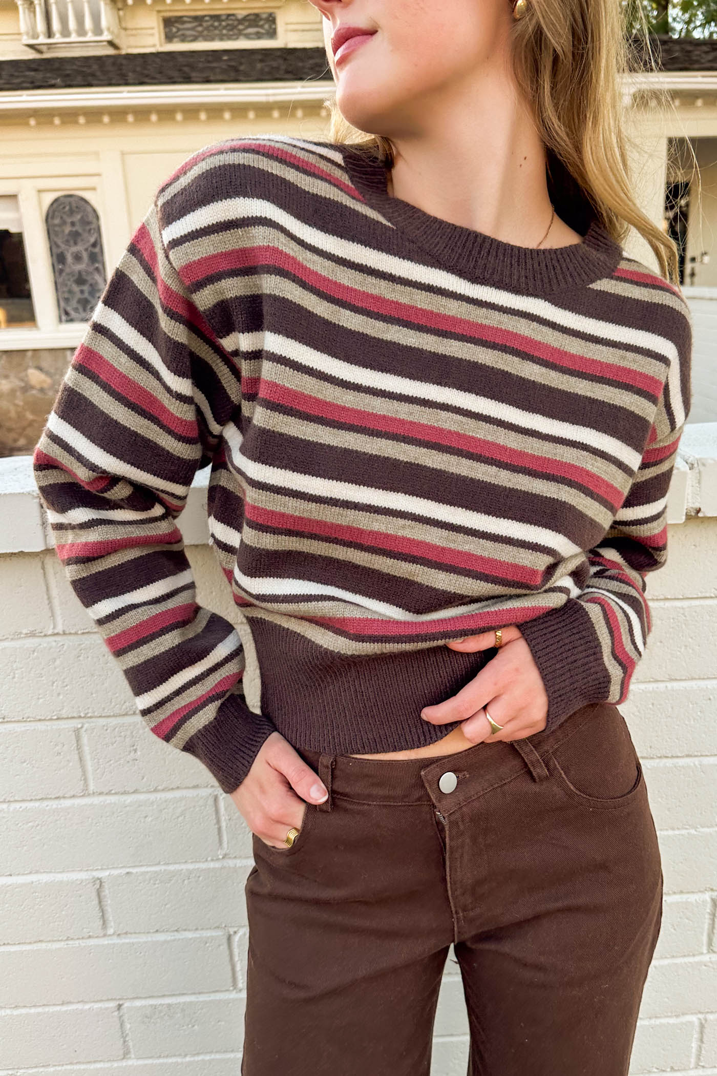 Person wearing a striped sweater and brown pants against a white brick wall.